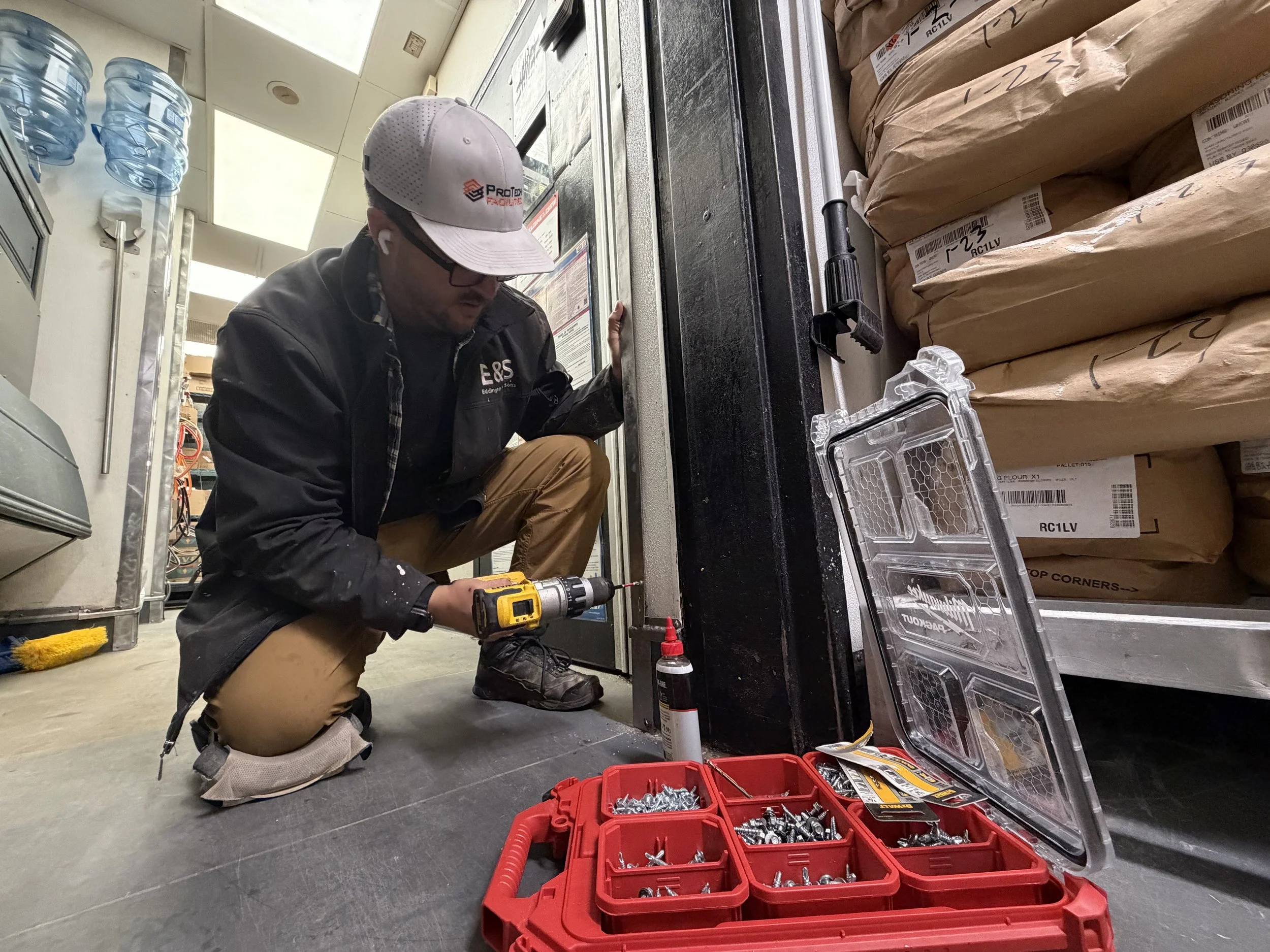 Commercial handyman performing door frame repair with a power drill at a quick service restaurant in Athens, Georgia, facility maintenance and interior metal trim work.