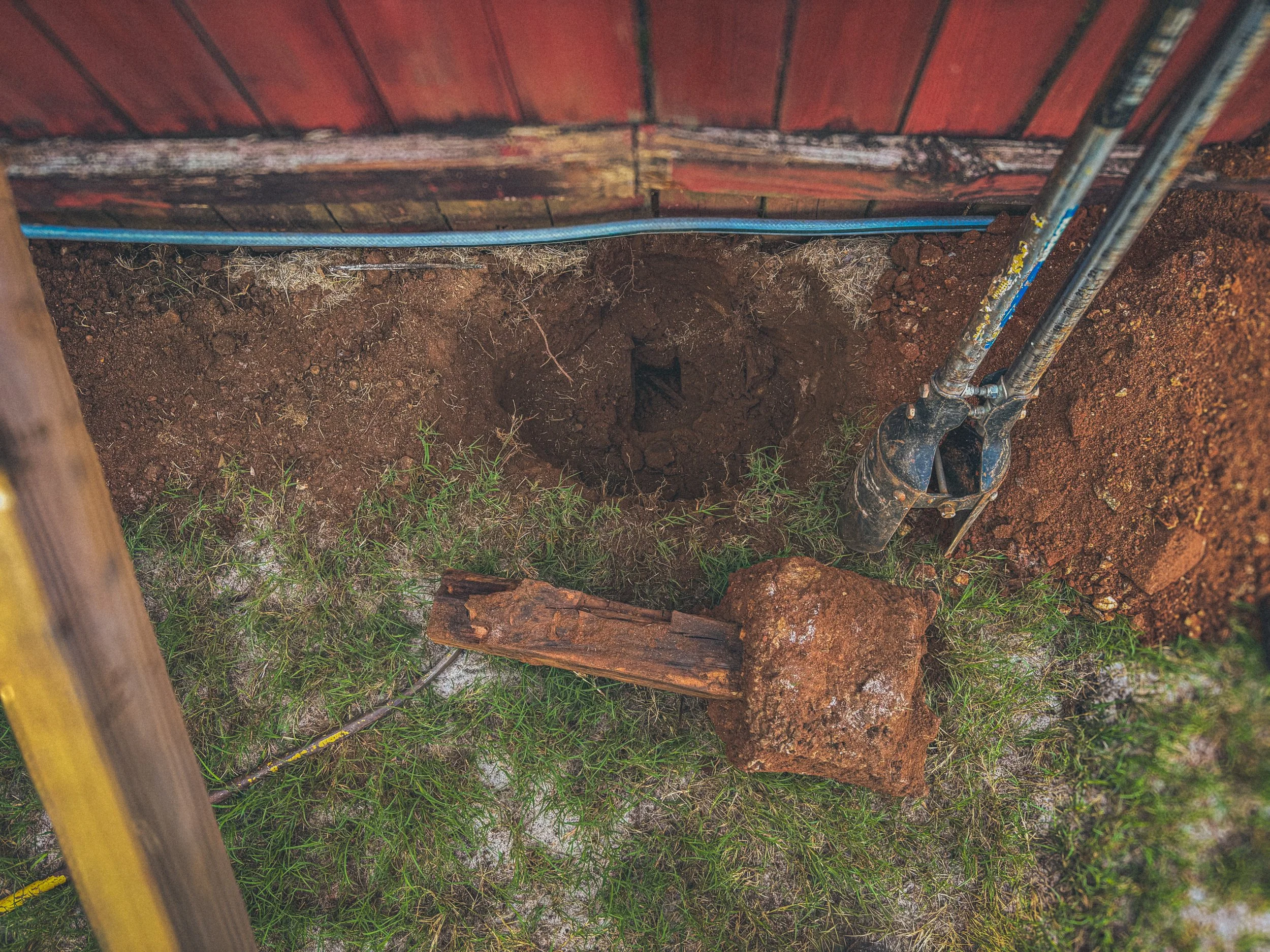 An old rotted post with the concrete footer still attached next to a huge hole in the ground it was removed from