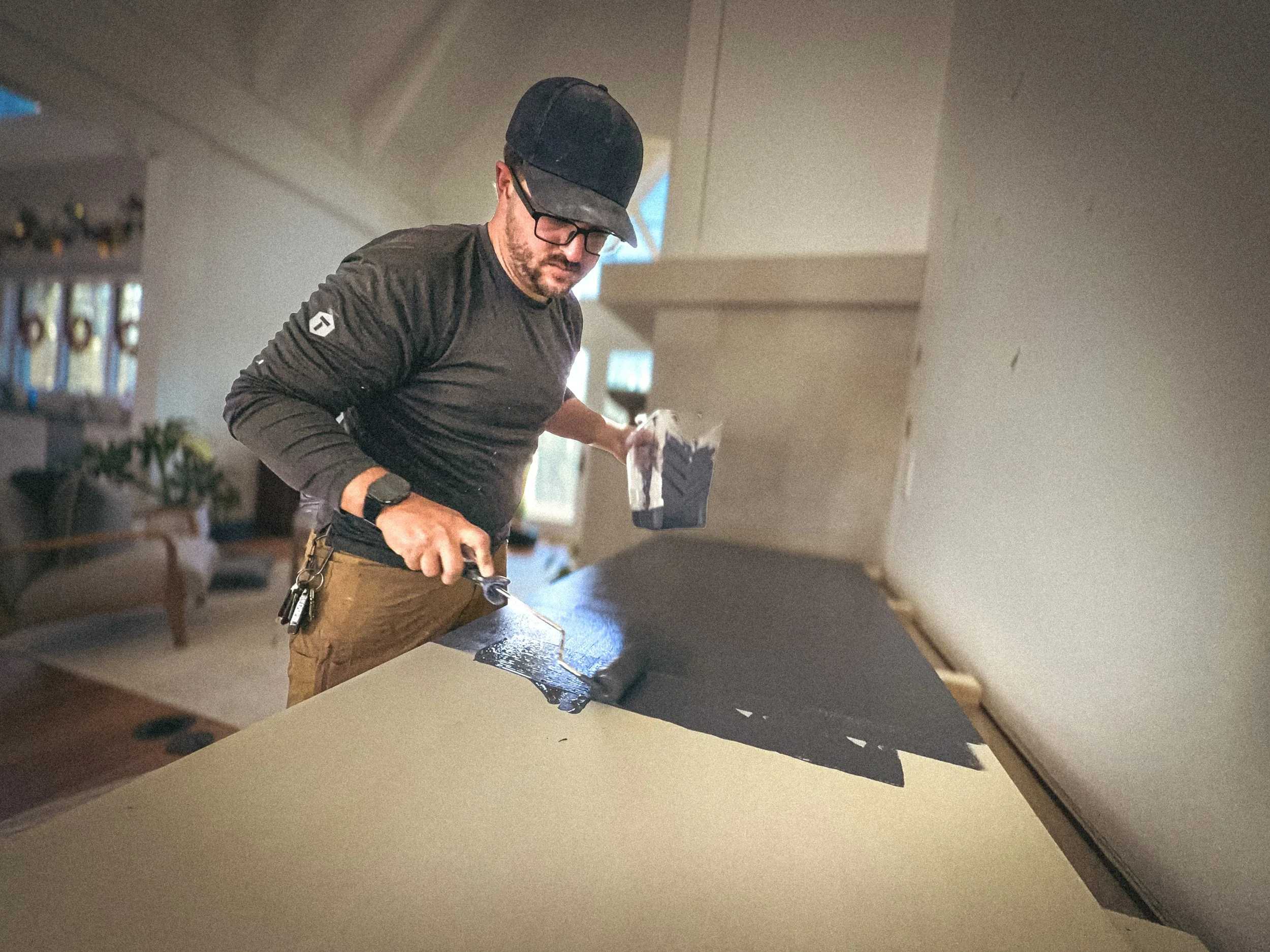 Handyman in Athens, GA applying a navy blue urethane enamel paint, to a wooden countertop in an interior residential space.