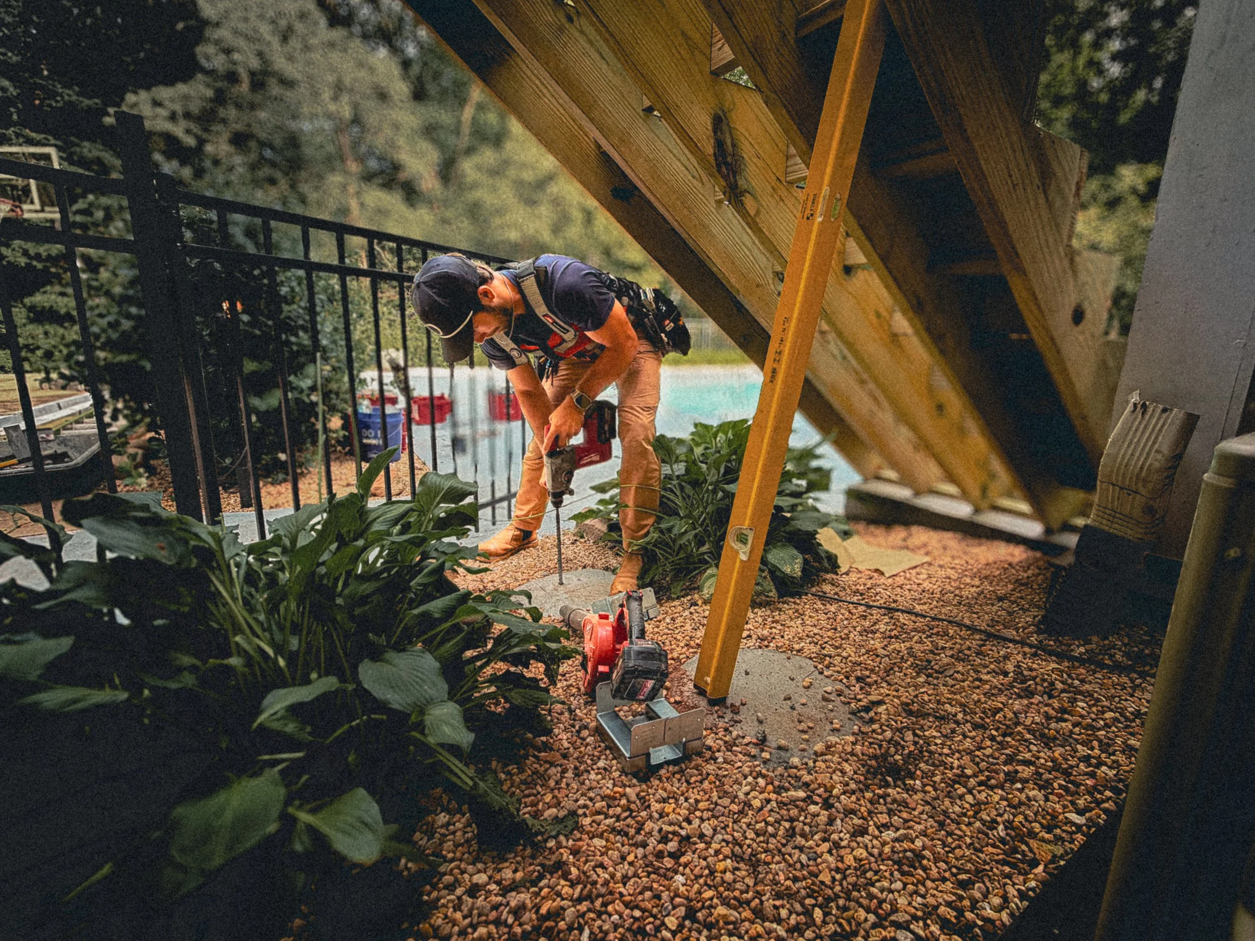 Carpenter using a SDS drill to make a hole in a concrete footer with post base sitting near by