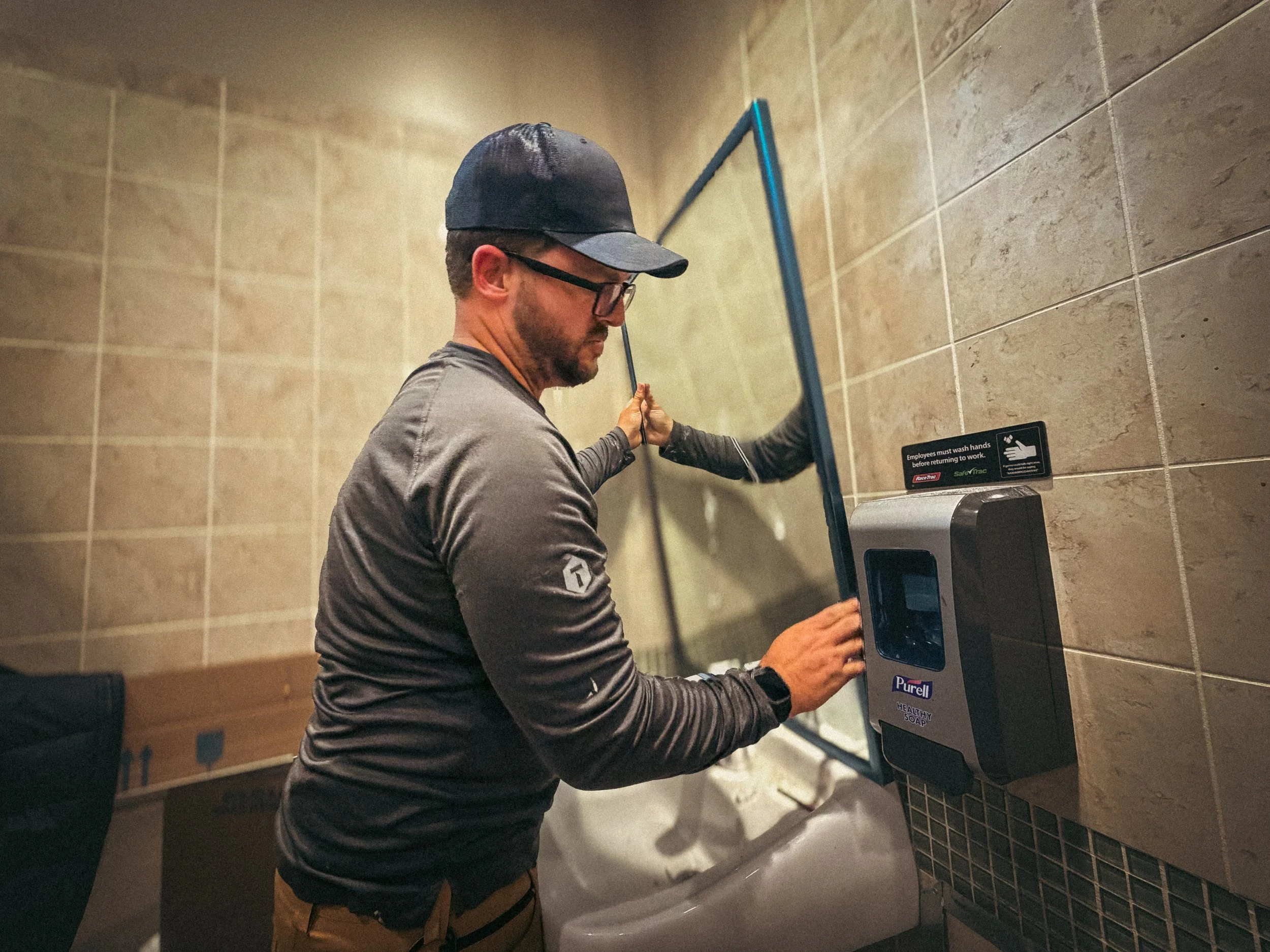 Commercial Handyman installing a new anti-theft commercial bathroom mirror at a gas station in Norcross, GA, performing retail facility maintenance and security upgrades