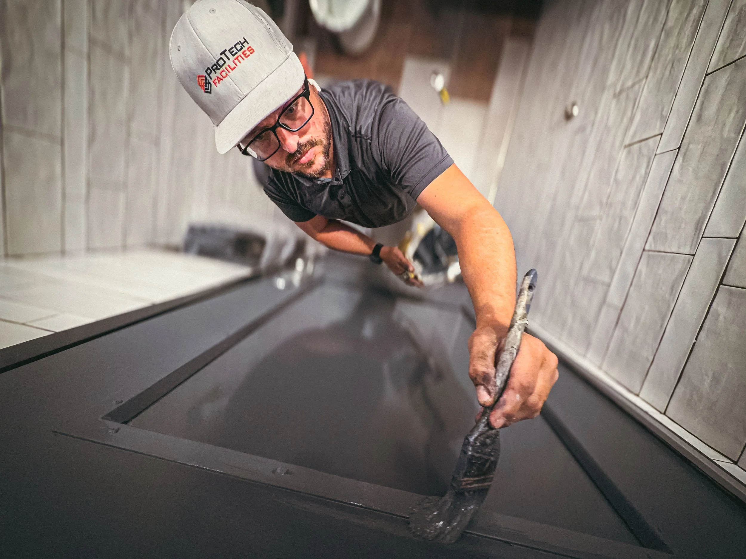 Commercial handyman applying paint to a bathroom door that is dark grey