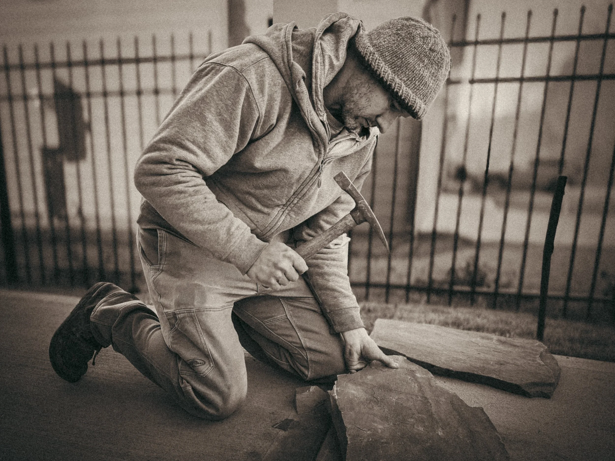 Hardscaper with a chipping hammer in one hand and flagstone in another