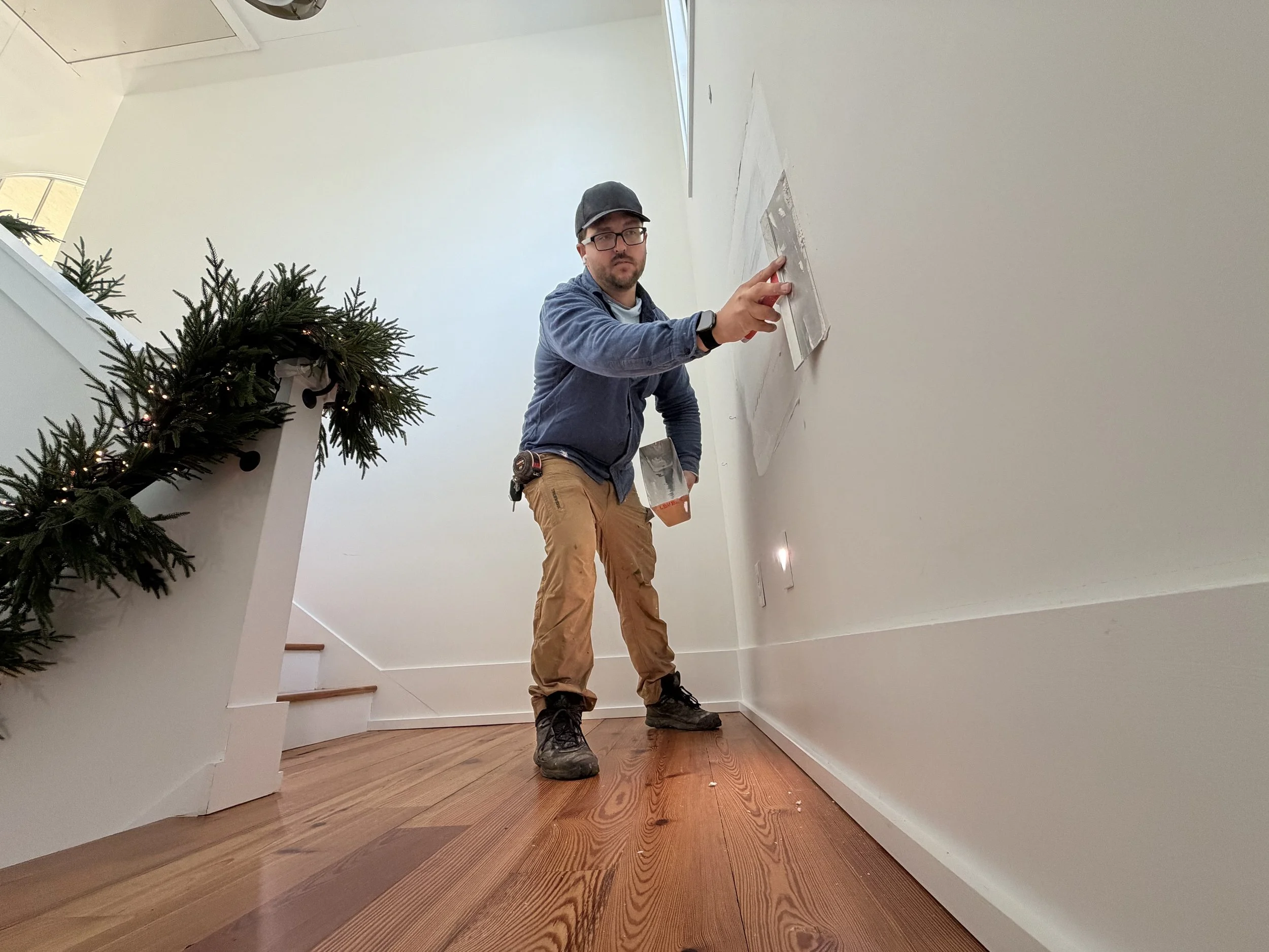 Handyman in Oconee County, Georgia applying drywall compound with a taping knife during an interior wall repair in a residential home.