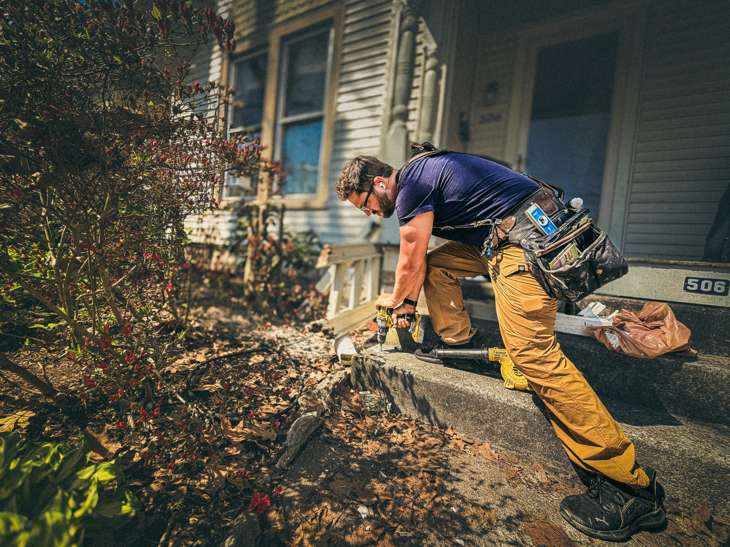 Carpenter drilling a hole into a concrete step to accept a post base for a handrail repair in Athens, GA