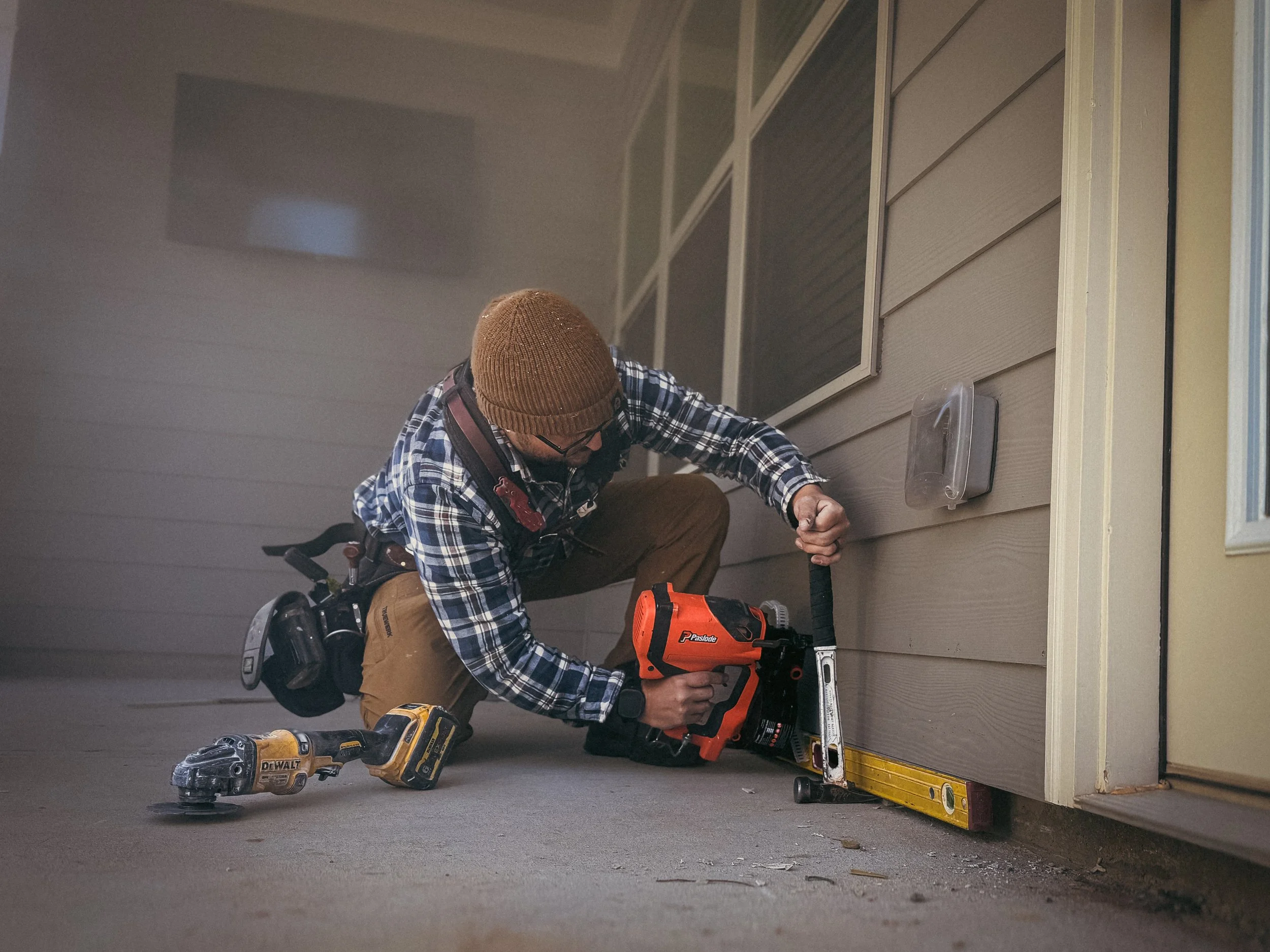Handyman in North Georgia, using a hammer to pry fiber cement siding level and fastening with an orange cordless paslode siding nailer