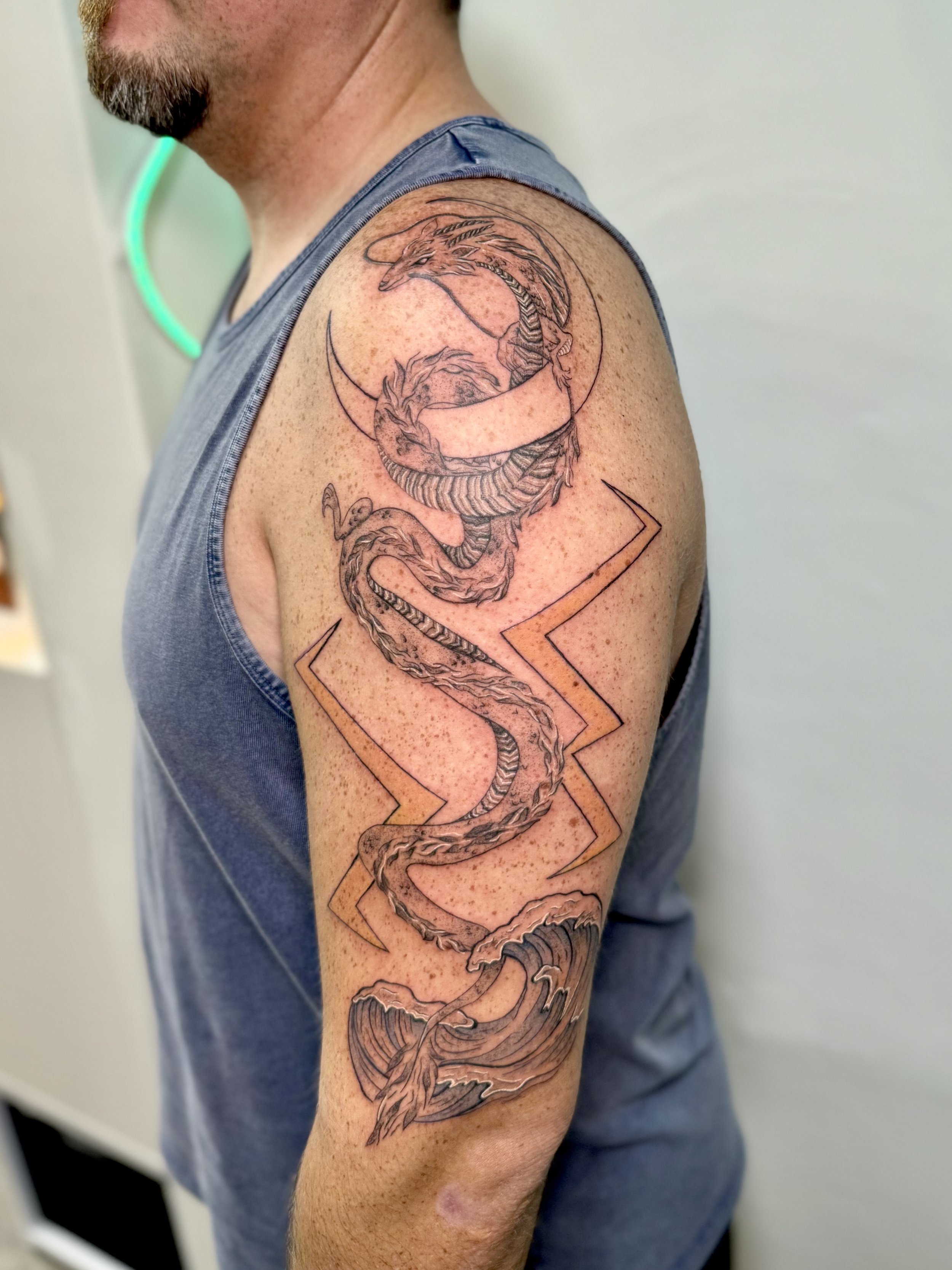 Tattoo of a dragon wrapped around a crescent moon with lightning bolts on the arm.
