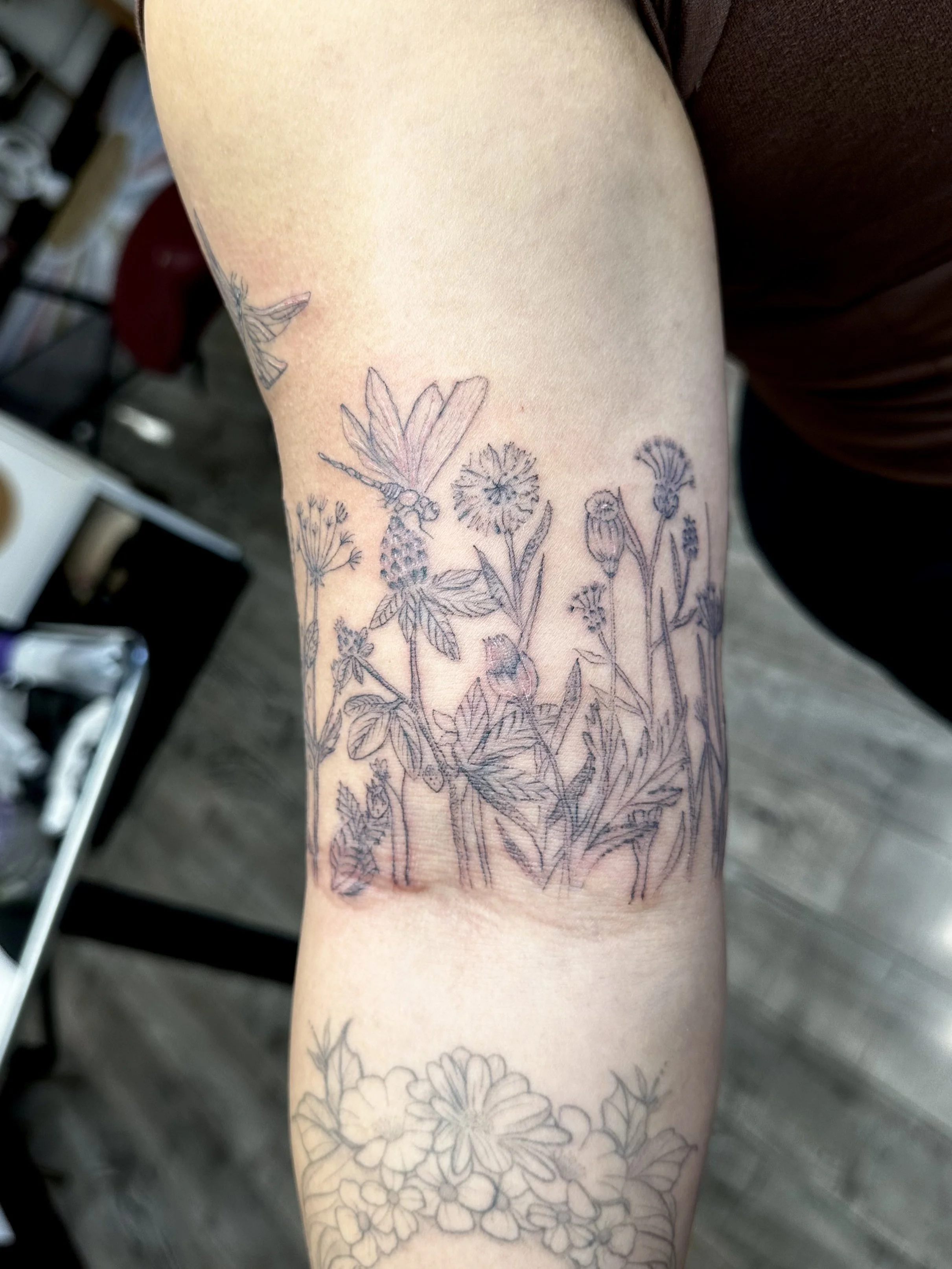 Tattoo of various flowers and a dragonfly on a person's forearm.