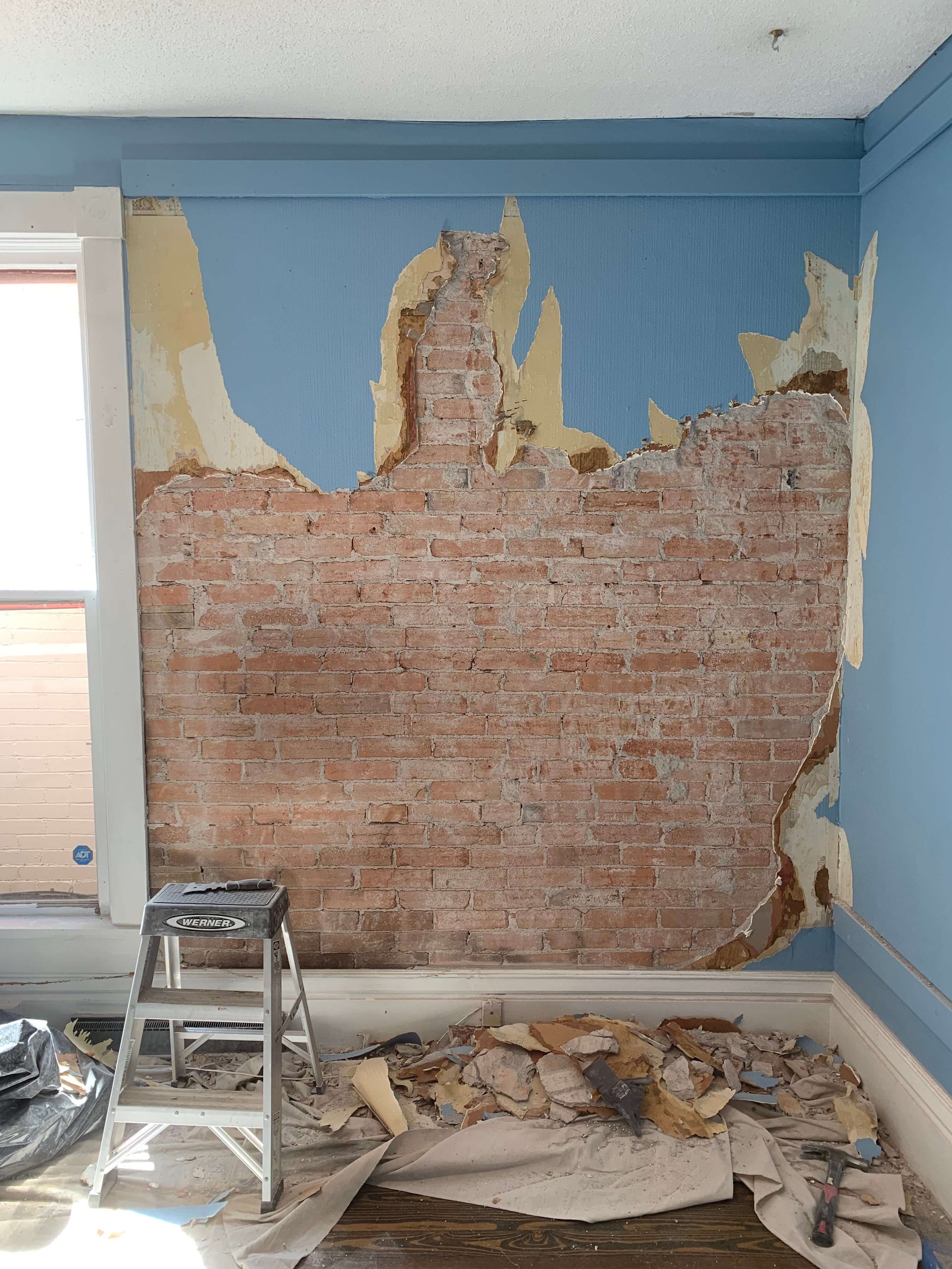 Removing 115 year old plaster with seven layers of wallpaper to expose the original brick. 