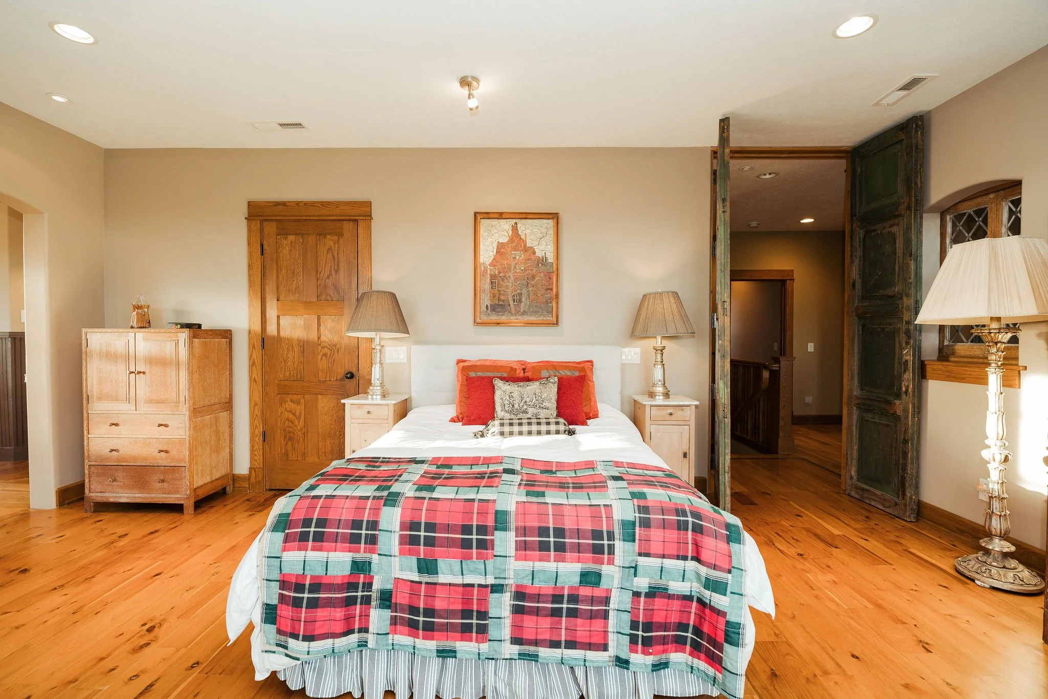 A cozy bedroom with wooden furniture, a bed with a plaid quilt and pillows, and warm lighting.