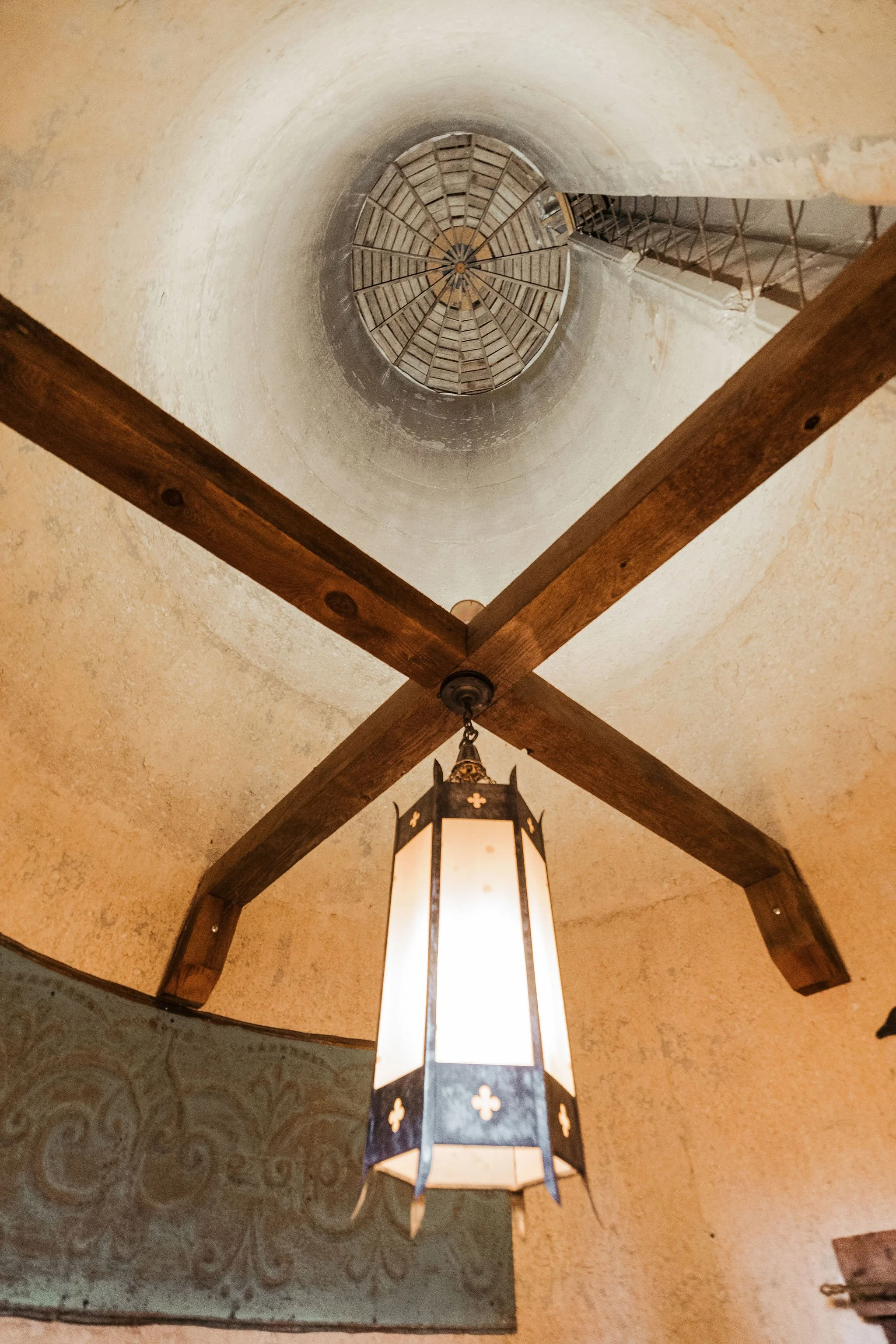 Ceiling with wooden beams, hanging lantern light, and a circular vent or skylight overhead.