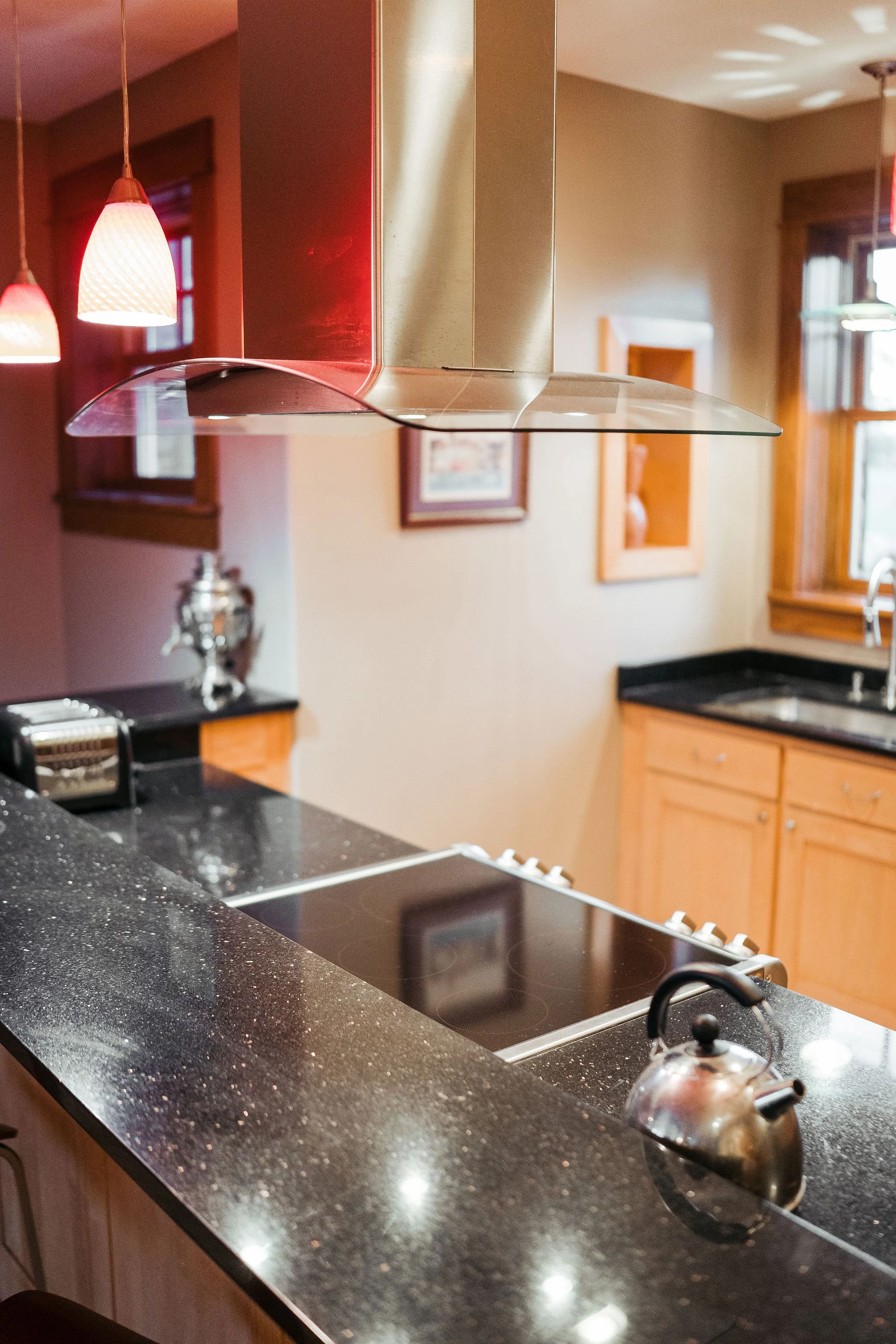 Kitchen with black granite countertops, a stainless steel kettle on the stove, a tea kettle on the counter, and hanging pendant lights.