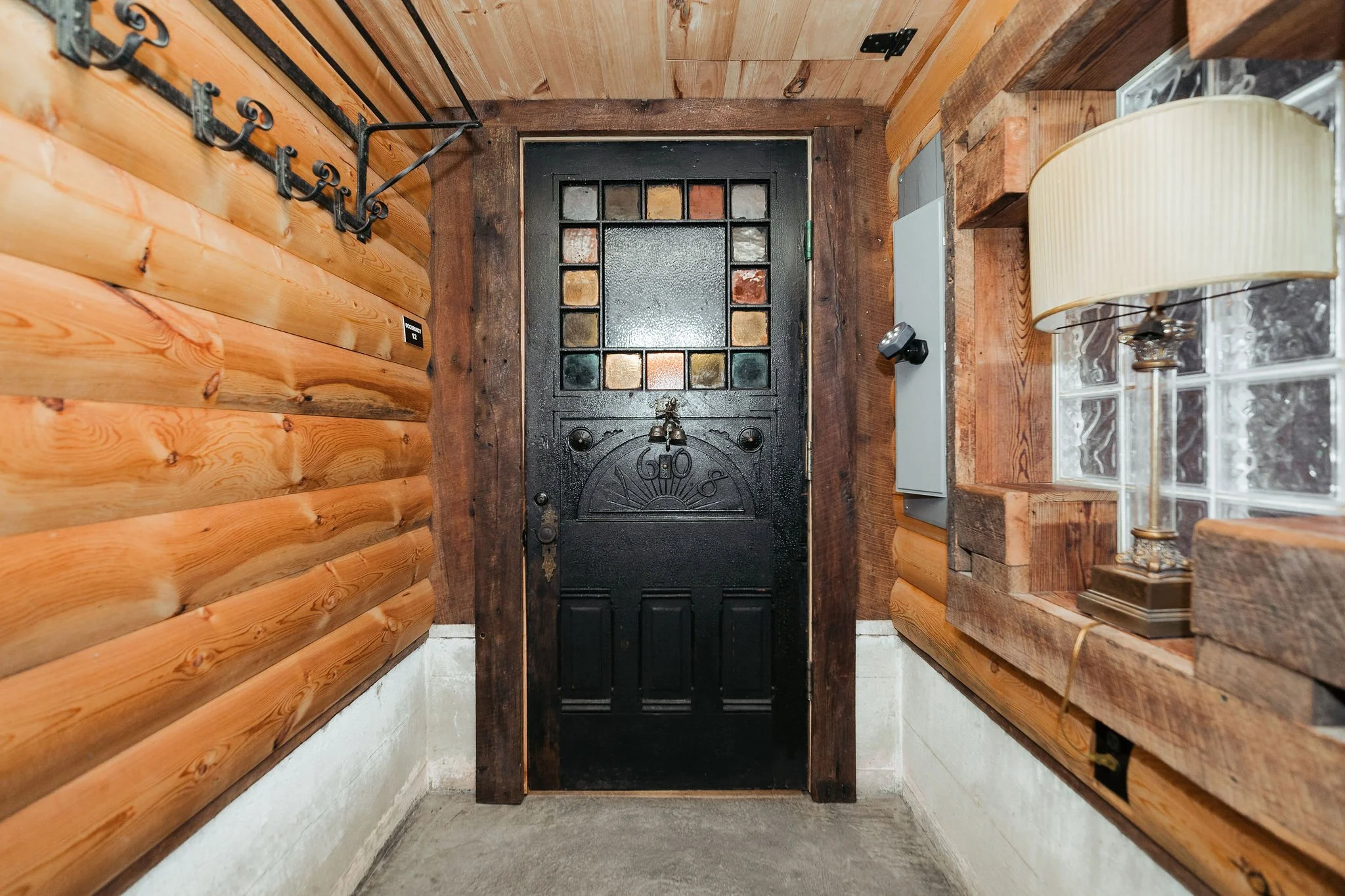 Entrance door with decorative stained glass window, surrounded by wood-paneled walls and a glass block window with a table lamp on the right.