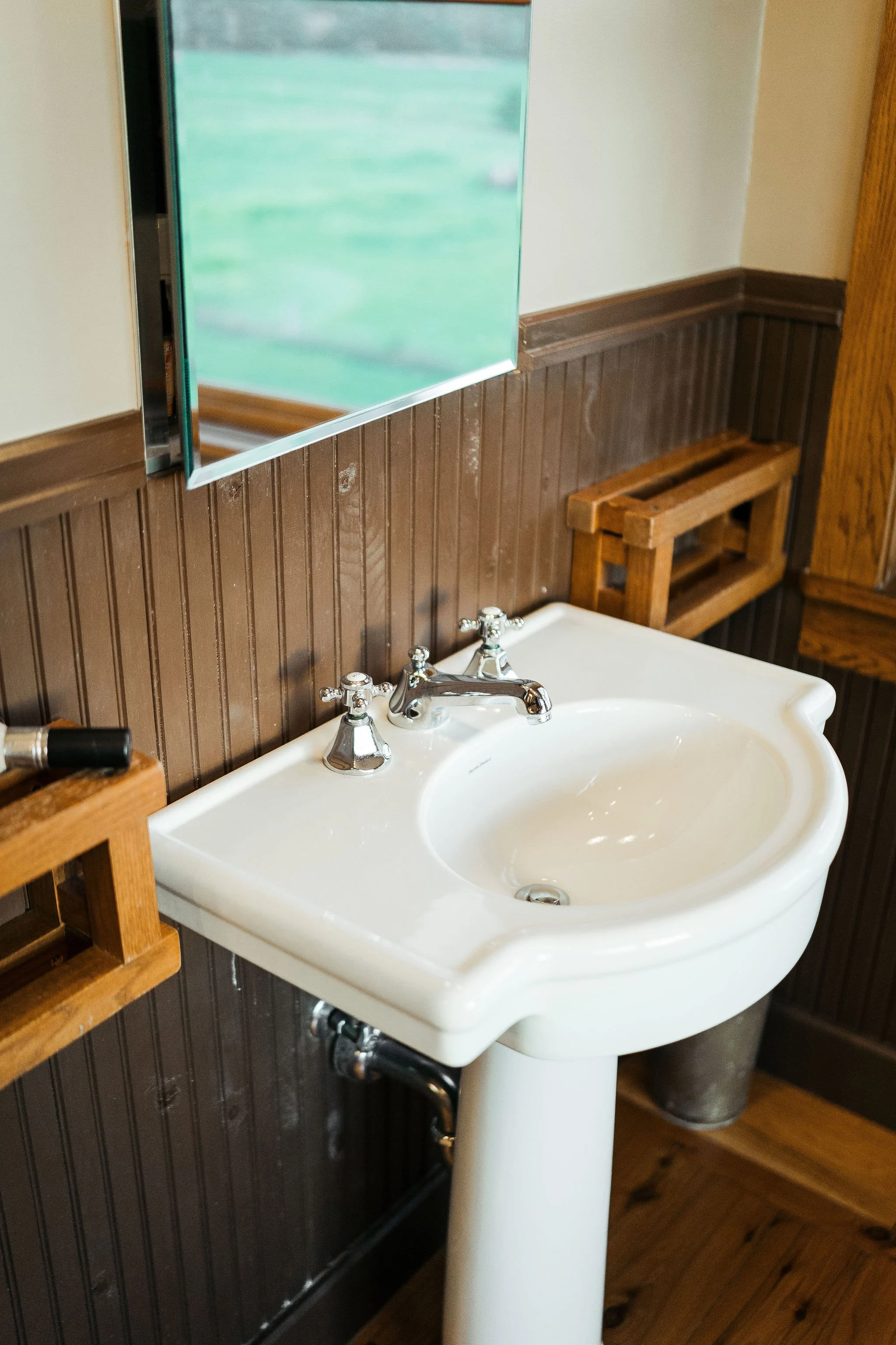 A white porcelain pedestal sink with chrome faucet in a bathroom with wooden accents and a brown wainscot wall.
