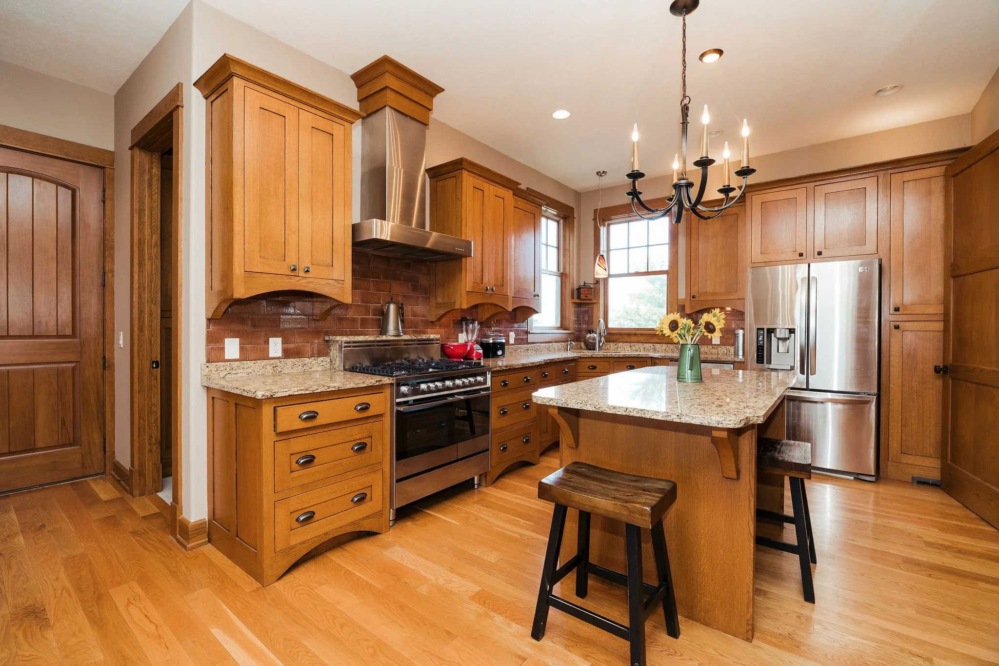 Kitchen with wooden cabinets, granite countertops, stainless steel appliances, a central island with a sunflower bouquet, windows, and a chandelier.