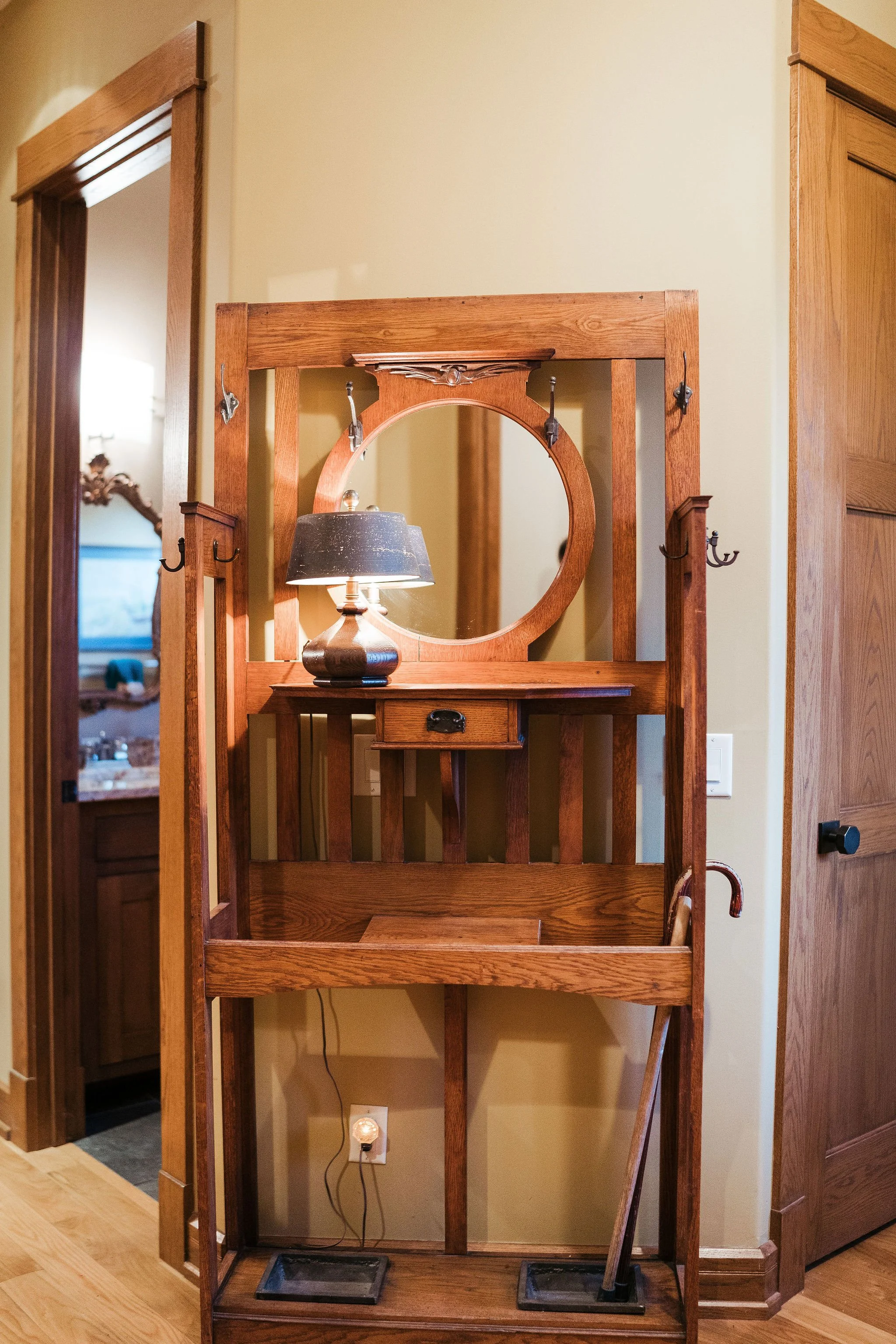 Empty wooden hall tree with hooks, a small drawer, a mirror, a lamp, and a cleaning tool leaning against it, located in a room with yellow walls and wooden floors.