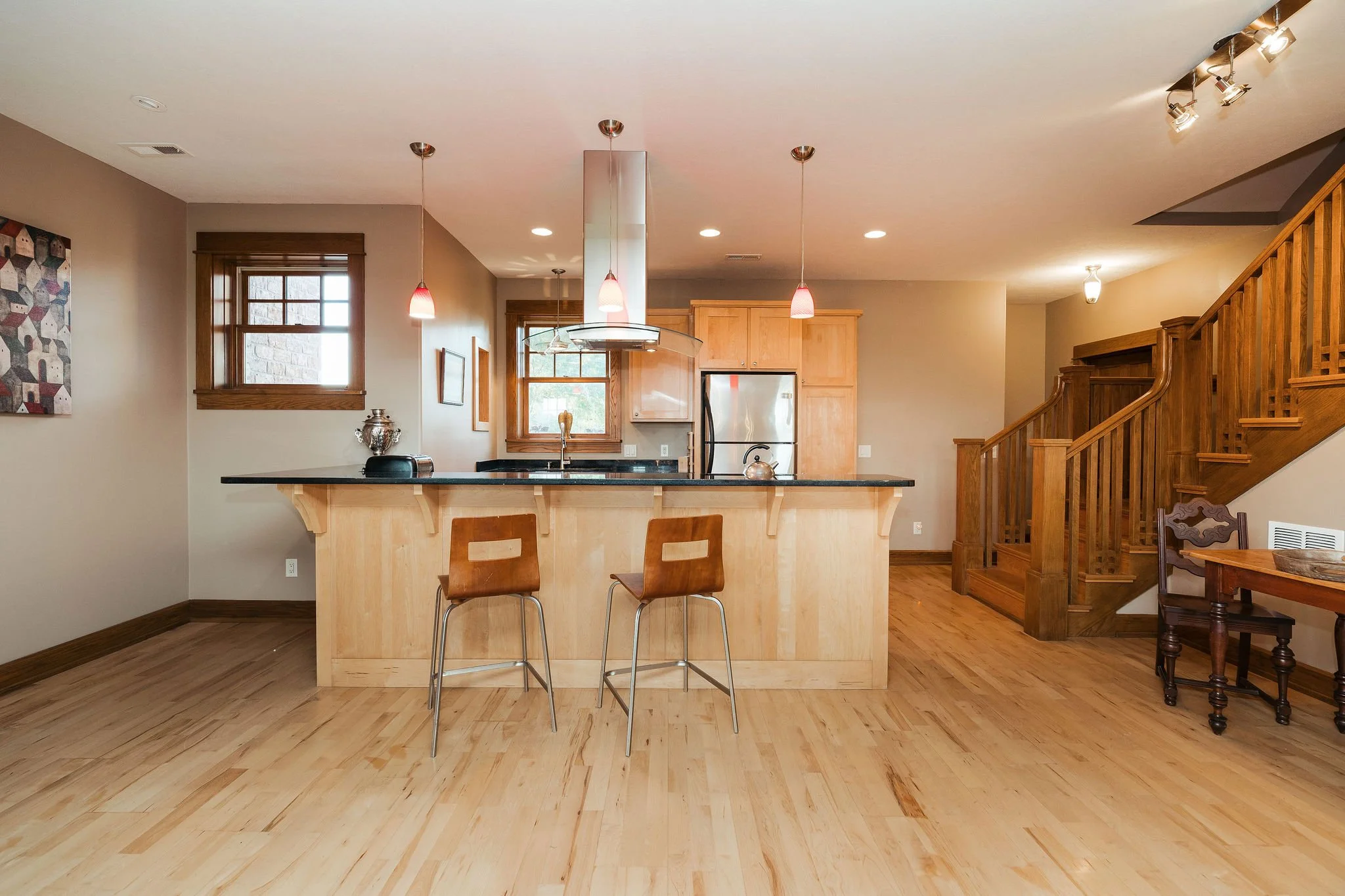 Open concept kitchen with wooden countertops, two brown chairs at the breakfast bar, stainless steel appliances, and wooden staircase to the right.