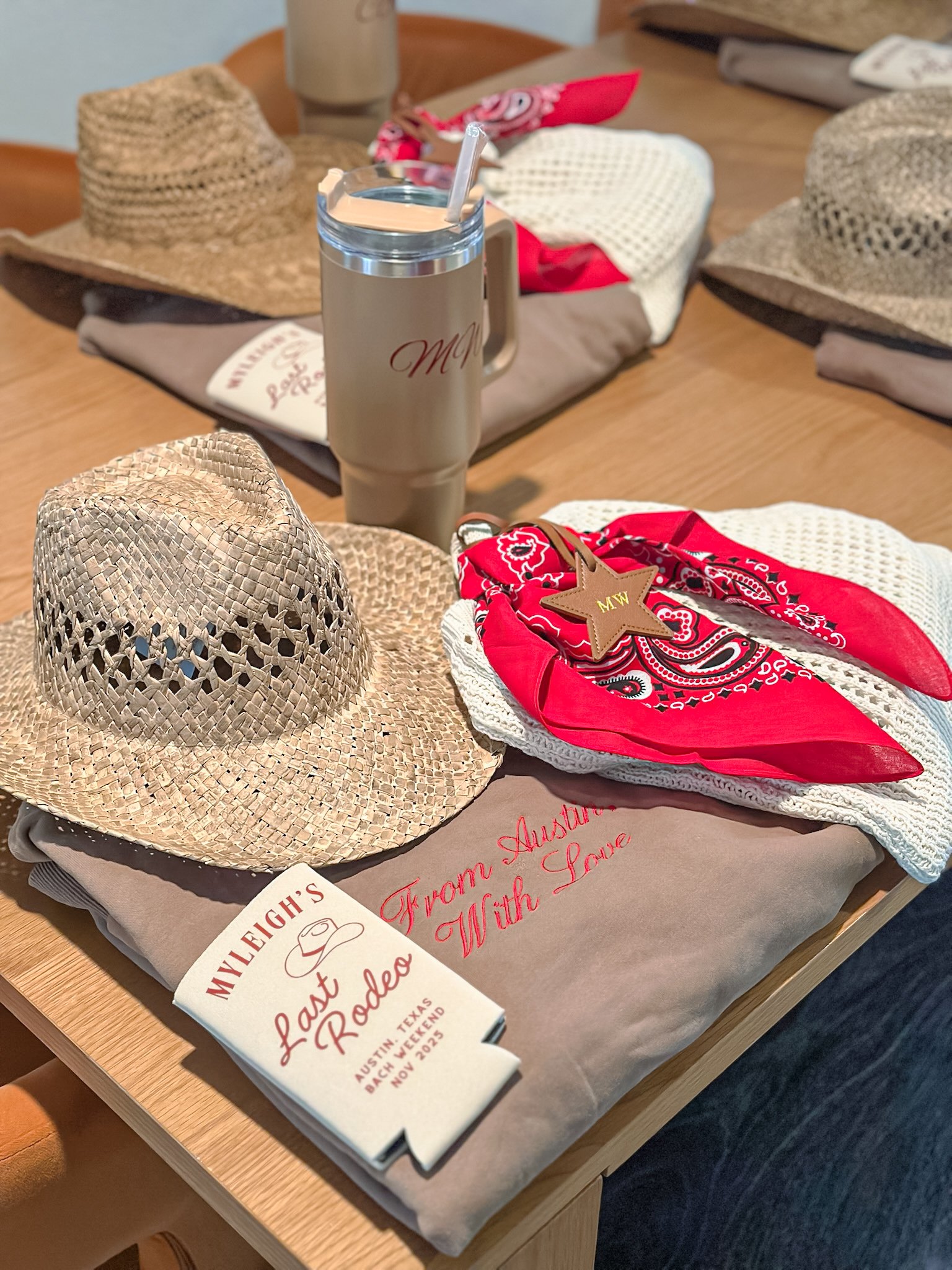 A table with straw hats, a red bandana, a tan mug with a straw, and a sign for the Lynd Flight Last Rodeo in Austin, Texas, November 2021.