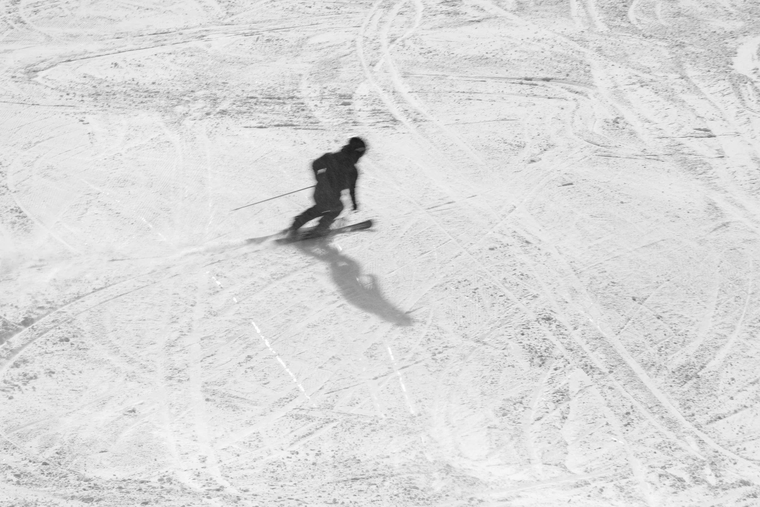 Persona esquiando en la nieve en una pista de esquí con rastros de esquí en el suelo, vista aérea en blanco y negro.