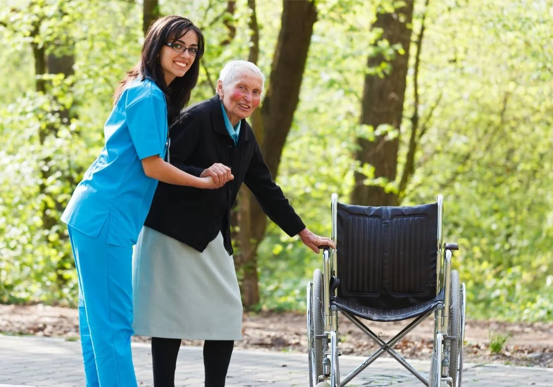 A caring healthcare professional holding hands with a patient preparing to sit in a wheelchair, symbolizing compassionate Non-Emergency Medical Transportation support in Northwest Arkansas.