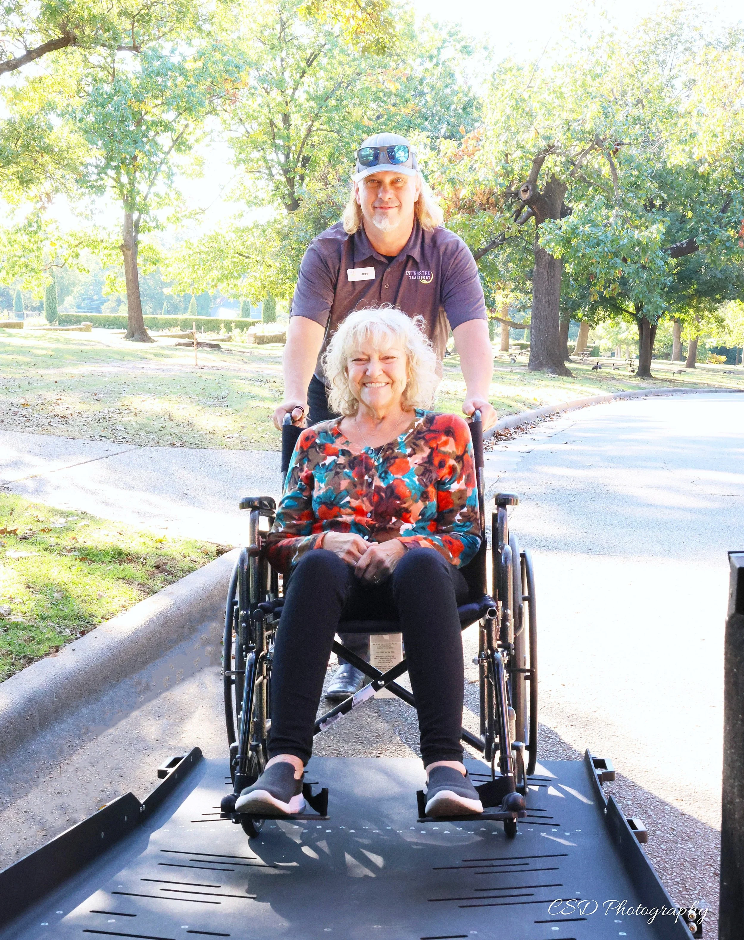 Entrusted Transport driver providing wheelchair assistance to a smiling senior woman outdoors in Northwest Arkansas.