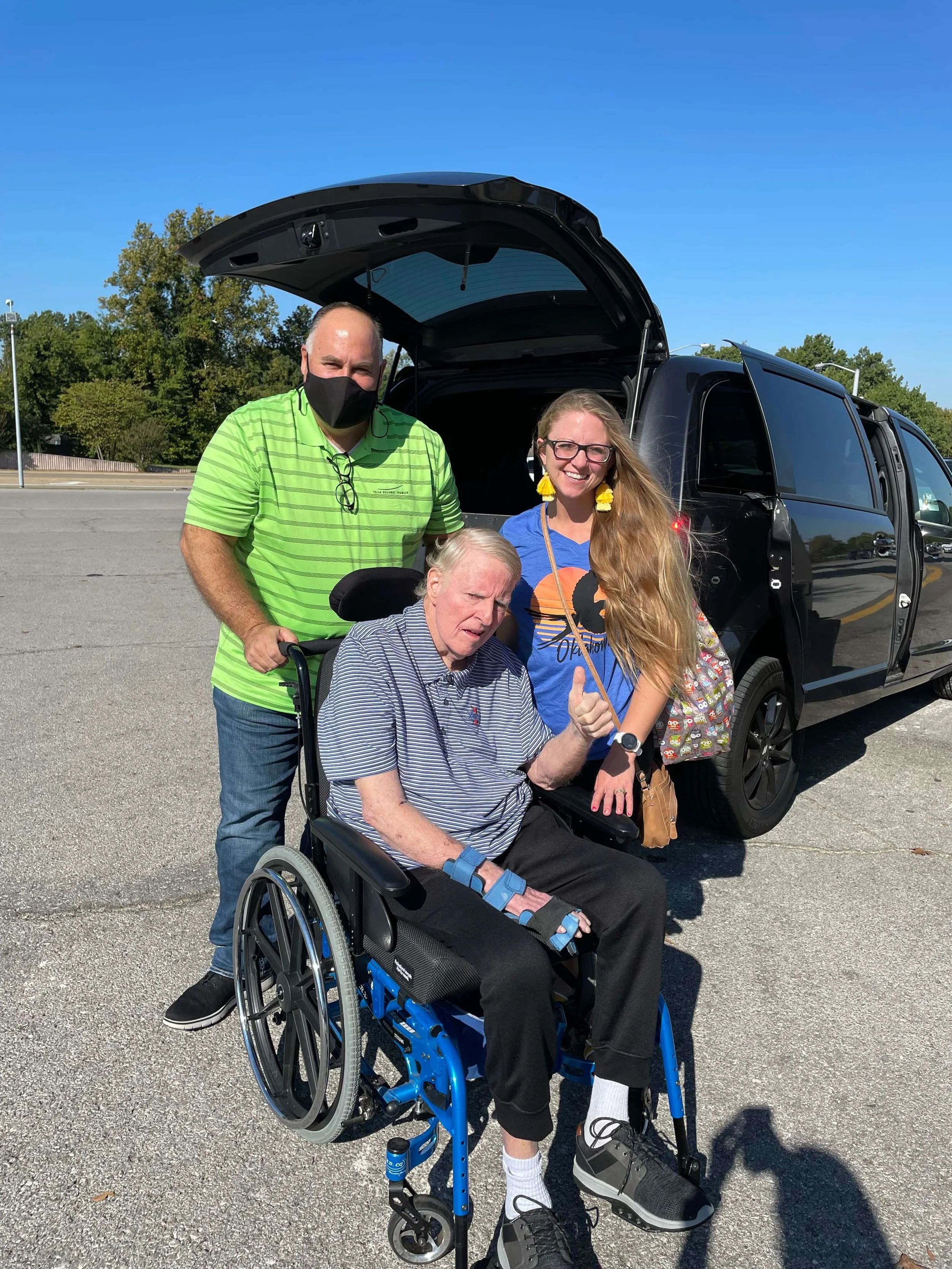 Owner assisting a patient in a wheelchair while speaking with a family member, representing compassionate and professional non-emergency medical transport.