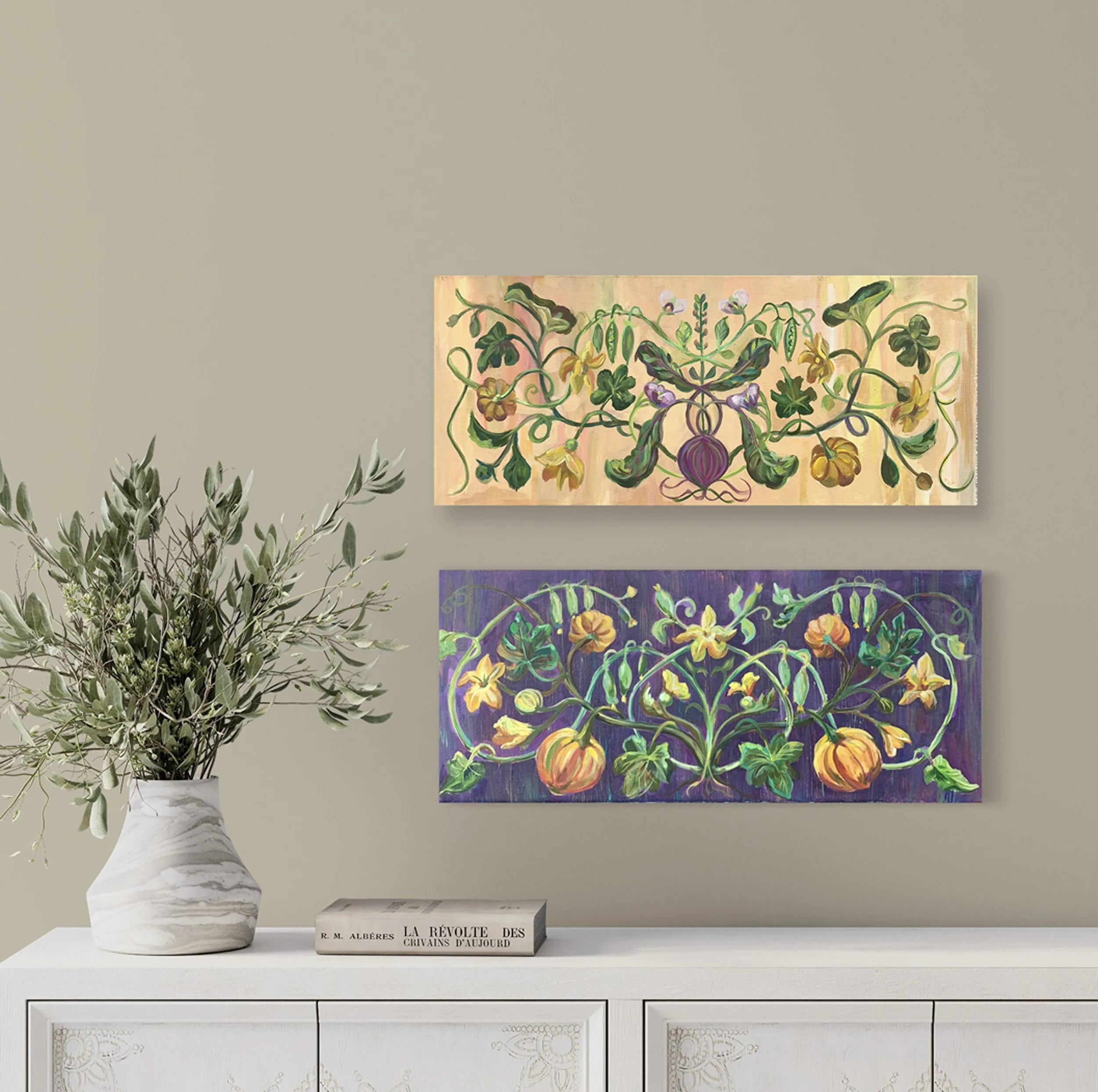 Two colorful paintings of plant motifs hang on a beige wall above a white sideboard. A marble-patterned vase with green foliage is on the sideboard, along with a book titled 'La Révolte Des Criavans D'Aujourd'hui'.