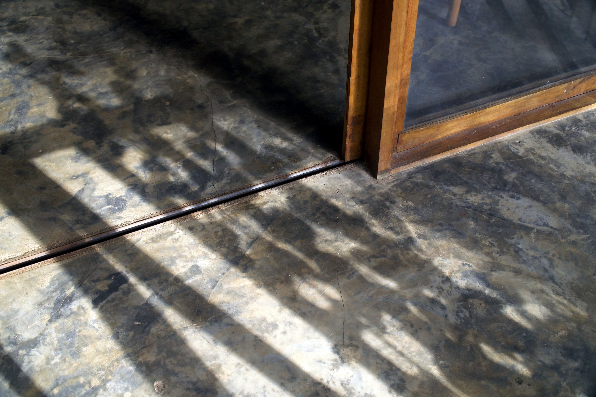 Sunlight casting shadows through the glass door of the island cottage onto a tiled floor.