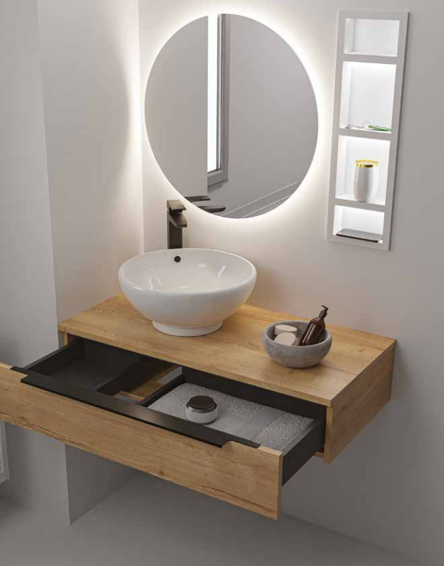 Modern bathroom vanity with a round white vessel sink, a round mirror, and a small wall shelf with a yellow and white container. The vanity is made of light wood, with a black integrated tray holding a soap dispenser and decorative items.