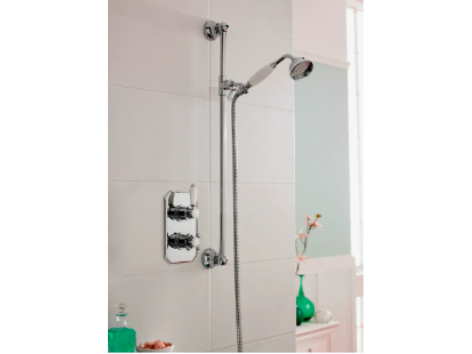 A modern shower with a handheld showerhead, chrome fixtures, and a soap dispenser on a nearby shelf in a bright bathroom.