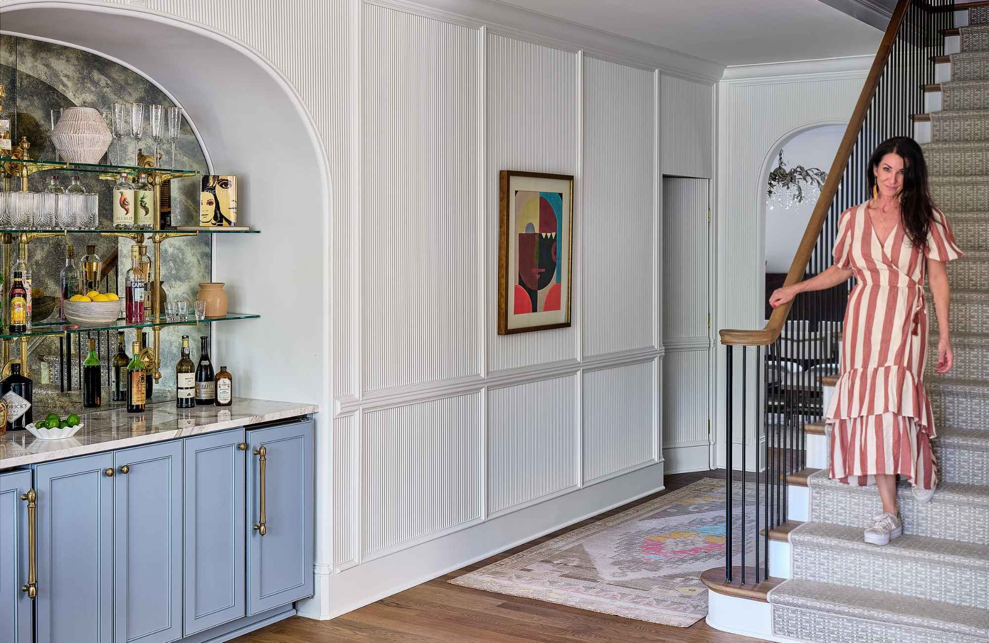 susan-hill-design-group-tega-cay-sc-interior-design-misconceptions-designer-walking-down-stairs-to-room-with-built-in-arched-bar-light-blue-cabinets-clean.jpg