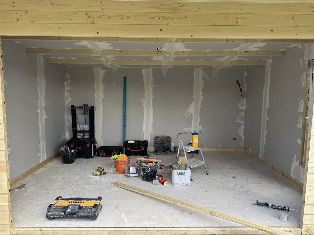 Room under construction with drywall partially installed, tools, and supplies scattered on the floor.
