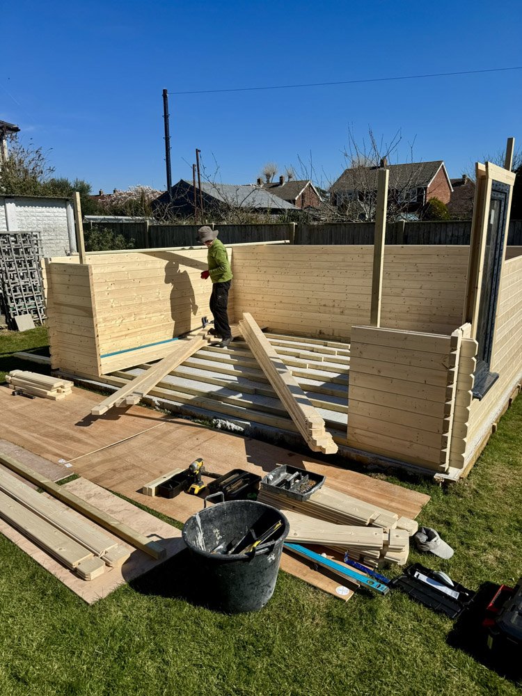 Child building a wooden fence in a backyard on a sunny day, with tools and materials scattered around.
