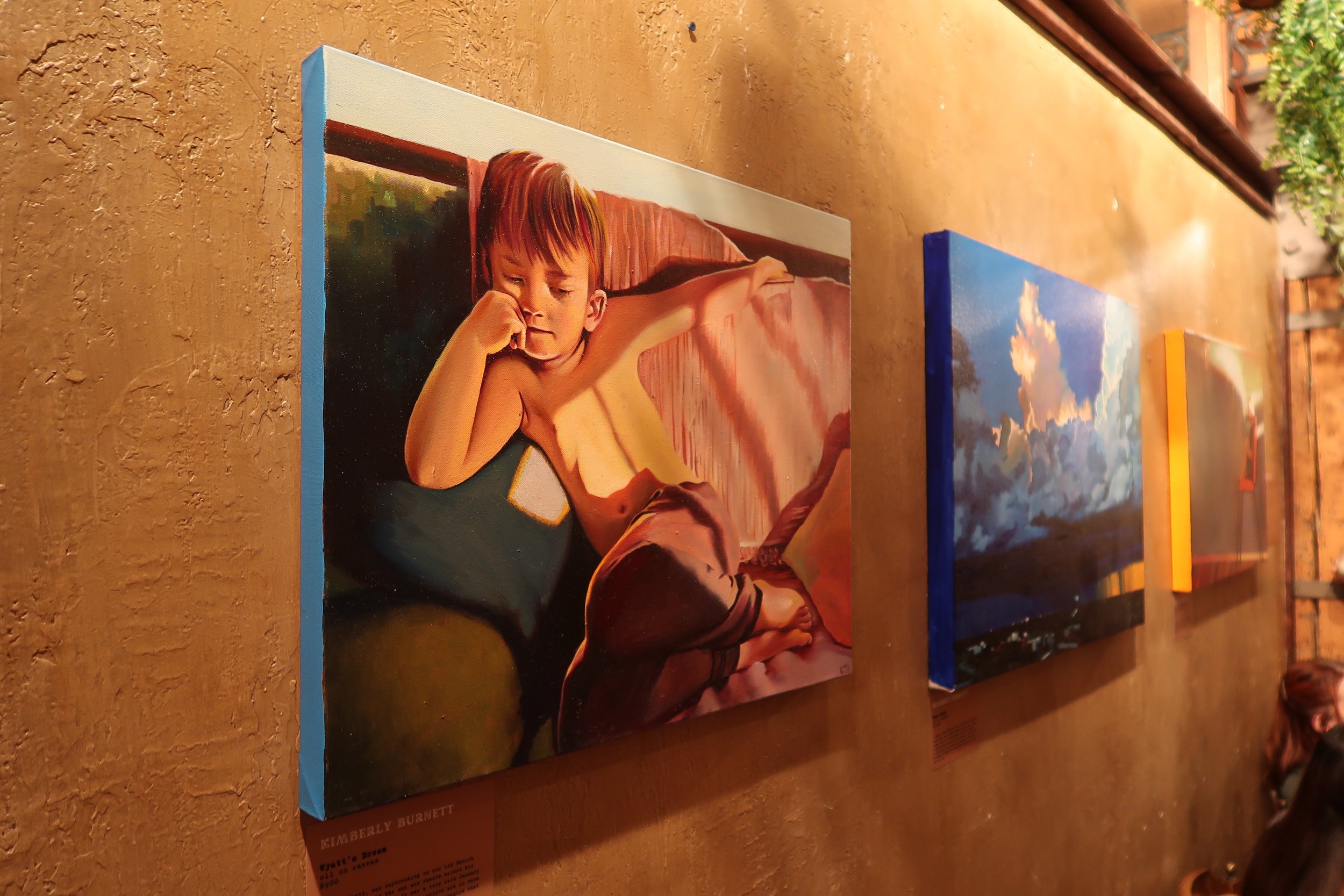  Oil paintings featuring a young portrait and a stormy landscape by artist, Kimberly Burnett, hanging at Hygge: A Pop Up Gallery, curated by Milwaukee artist, Lauren Marie Nitka, at  Glassnote Candle Bar , Walker’s Point, WI. 