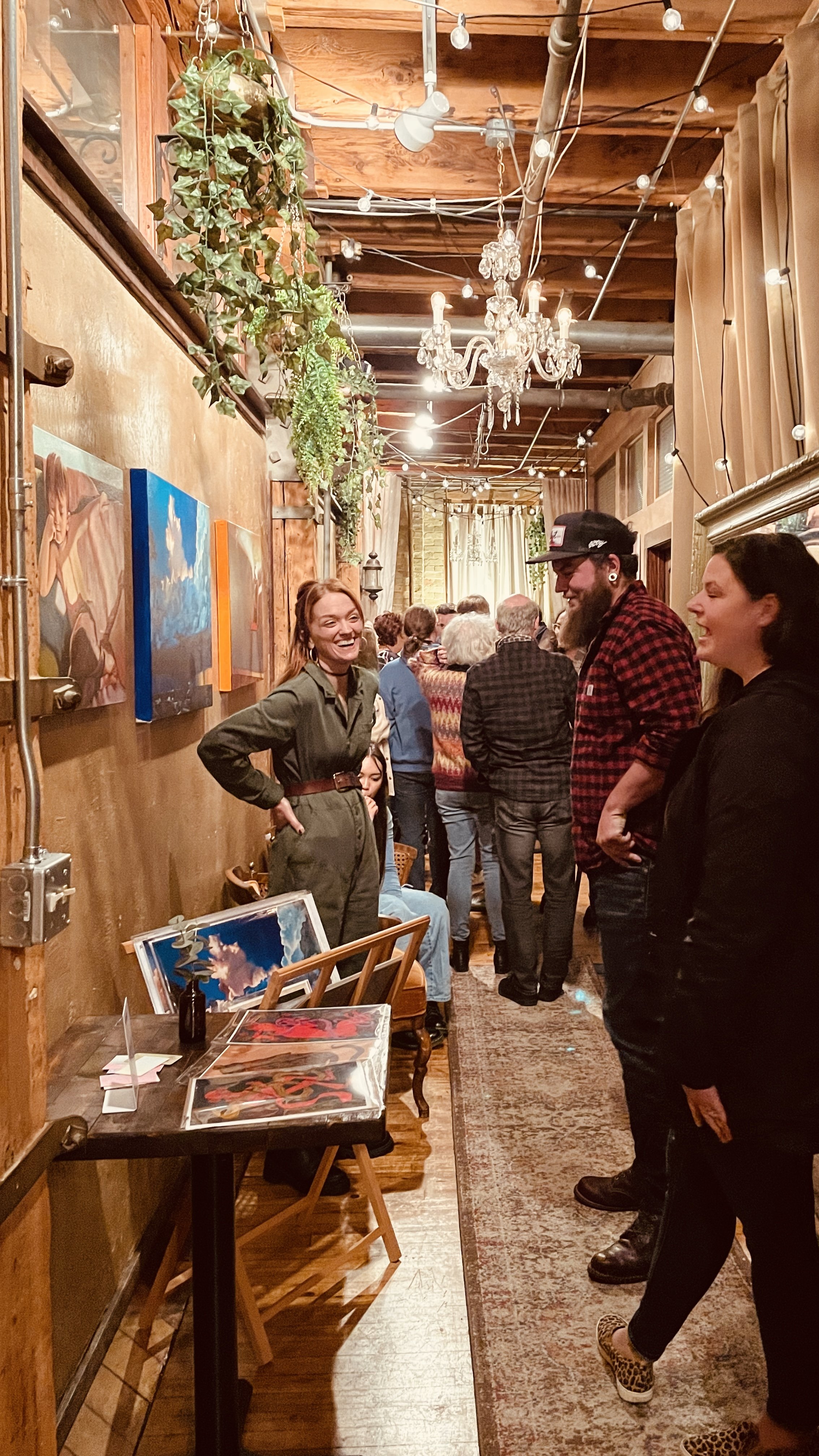  Artist  Kimberly Burnett  stands in front of her paintings, talking with guests at Hygge: A Pop Up Gallery, curated by Milwaukee artist, Lauren Marie Nitka, at  Glassnote Candle Bar,  Walker’s Point, WI. 