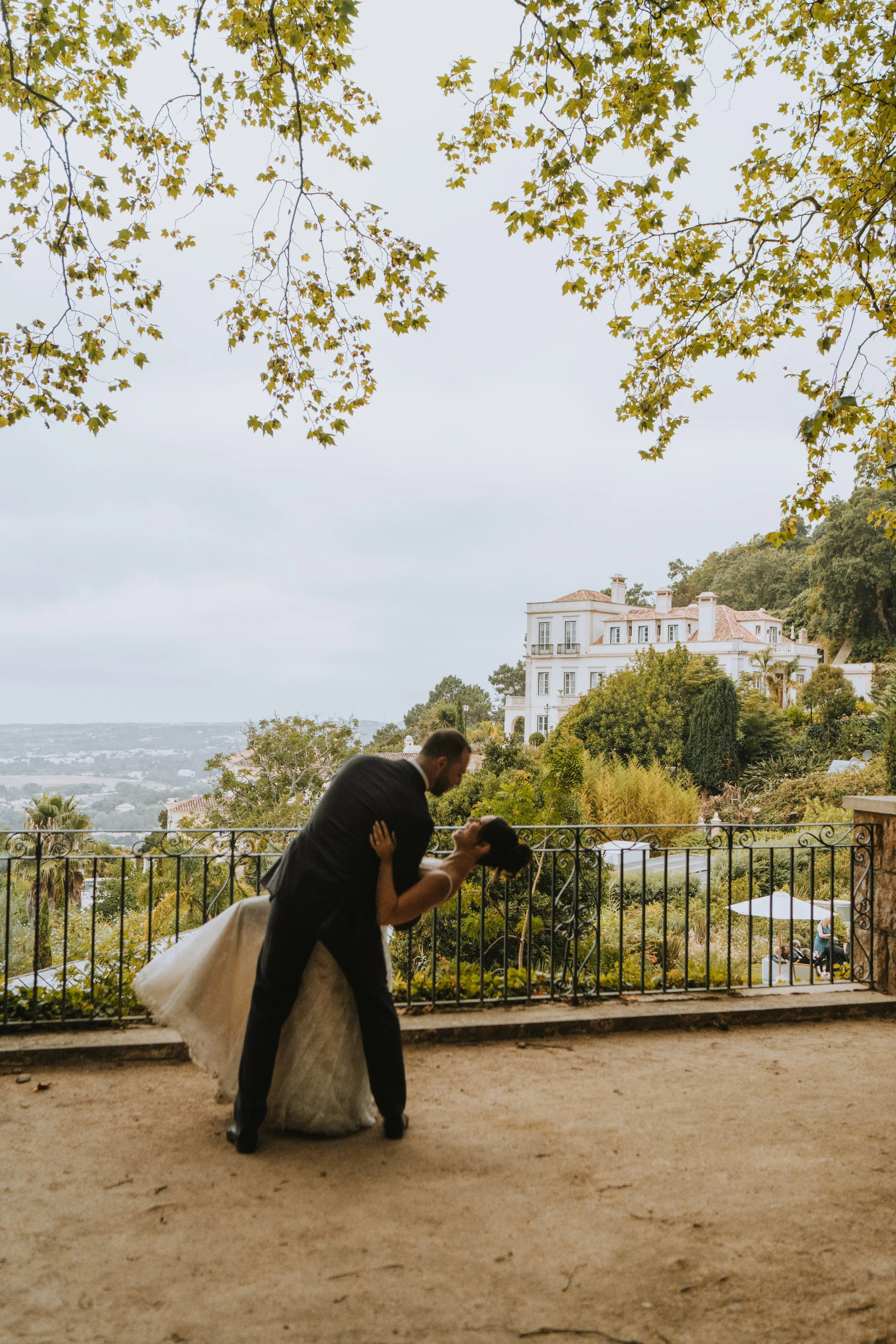 A couple dancing on a terrace with a scenic view of greenery and large white house in the background.