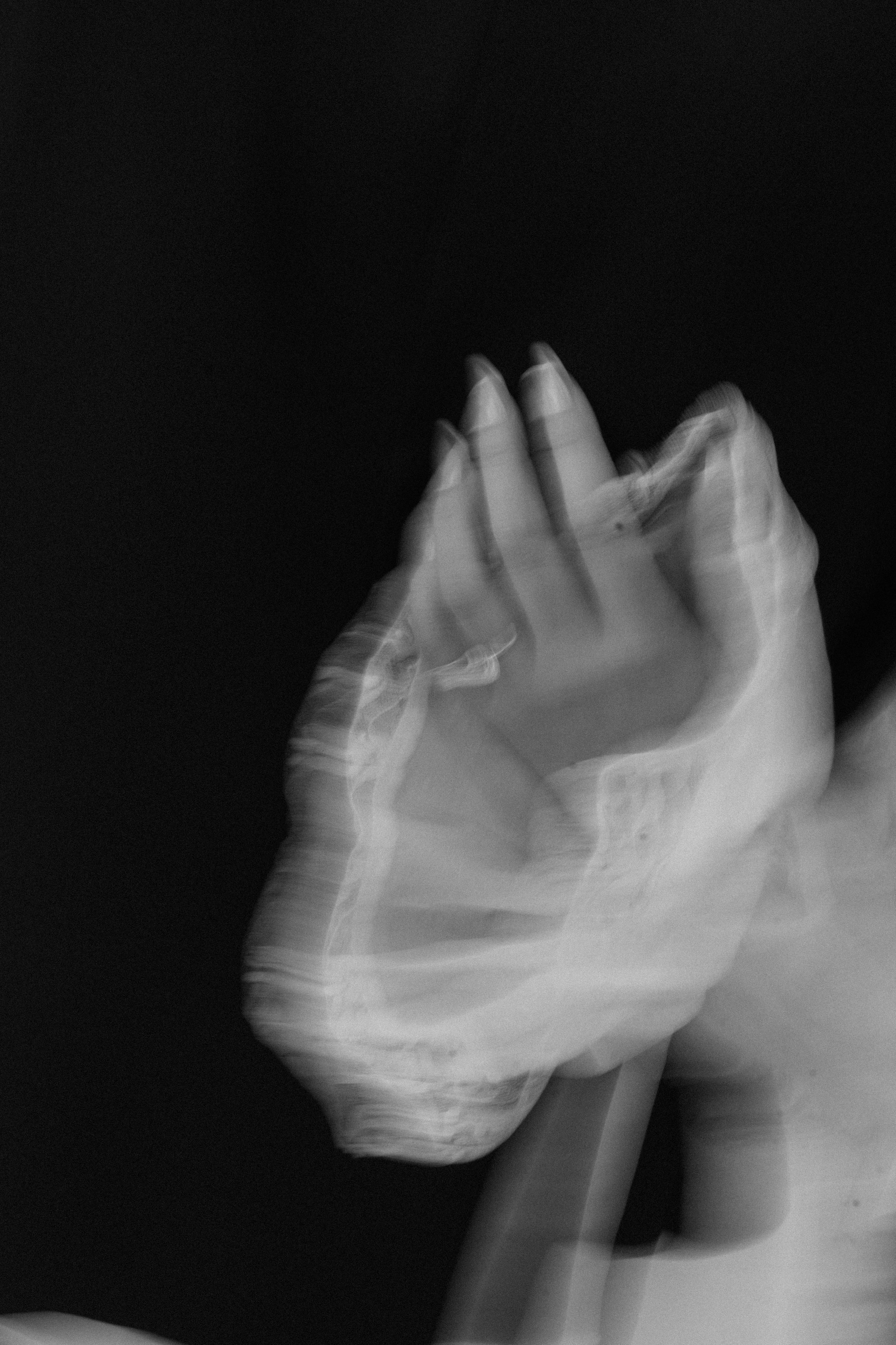 A black and white photo of a hand with motion blur, making a gesture with fingers close together against a dark background.