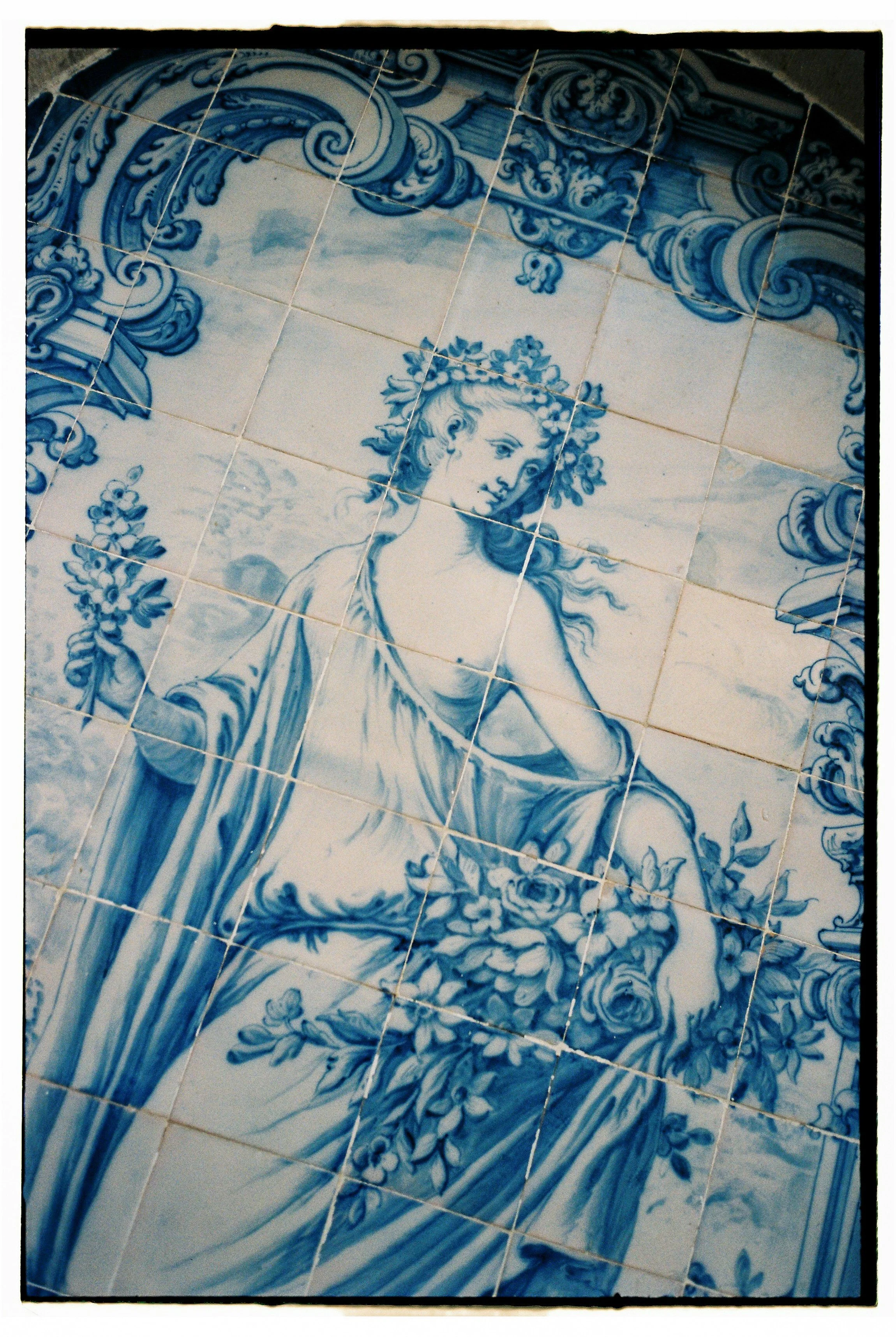 Blue and white ceramic tiles depicting a classical woman holding flowers, with intricate floral and scroll motifs in the background.