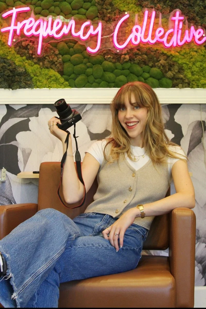 Portrait of Camryn Cassidy sitting in a chair under the Frequency Collective salon sign in Edmonds, WA