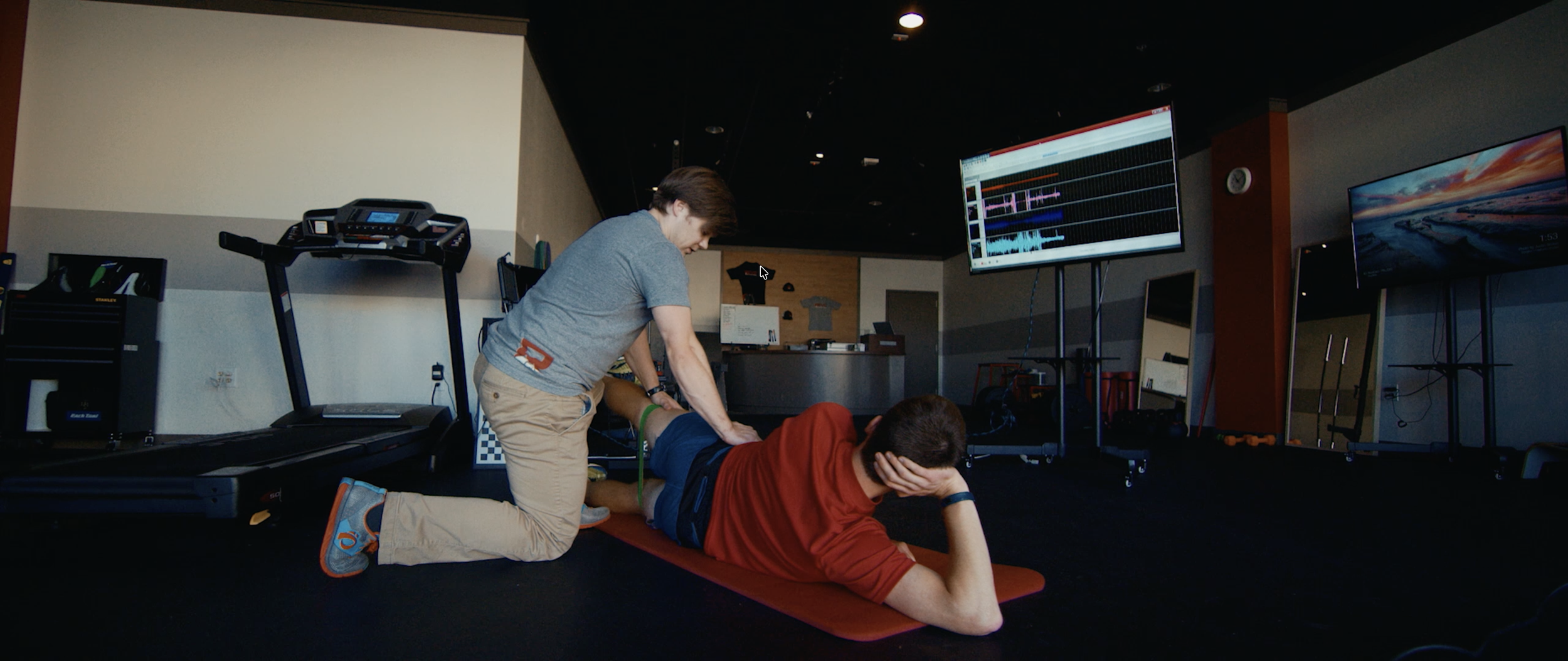 Person performing CPR on another person lying on a mat in a gym or fitness center.