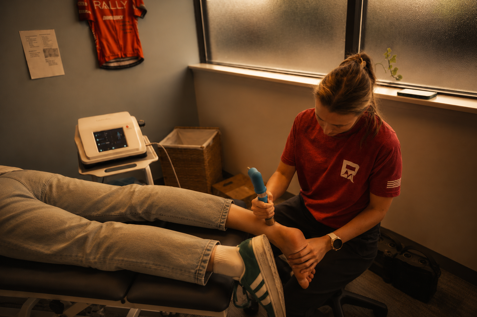 A healthcare professional using a handheld ultrasound device on a patient's ankle in a treatment room.