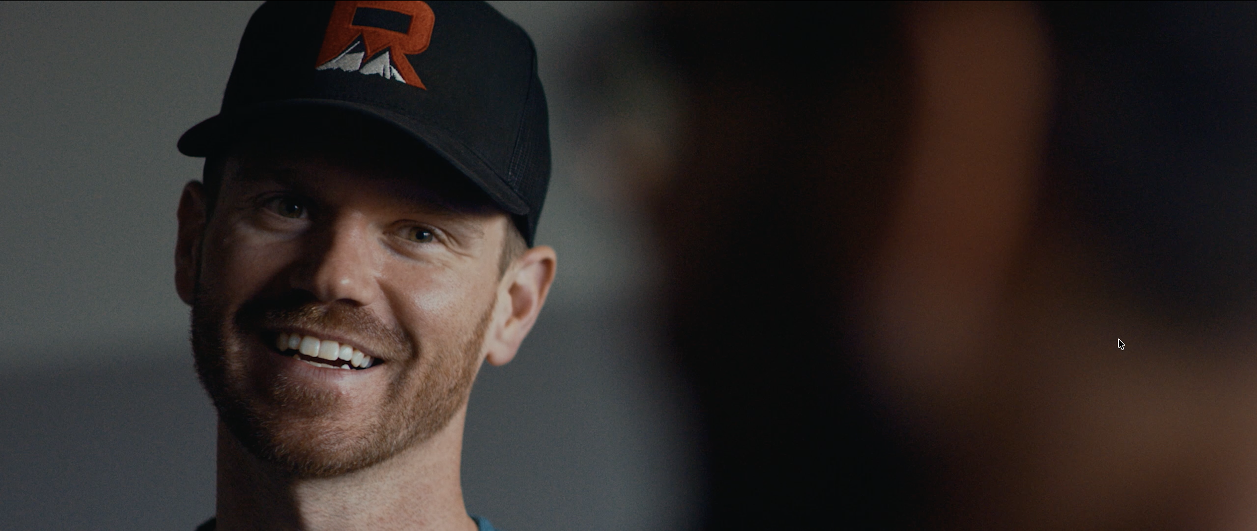 A smiling man wearing a black baseball cap with a red and white logo.
