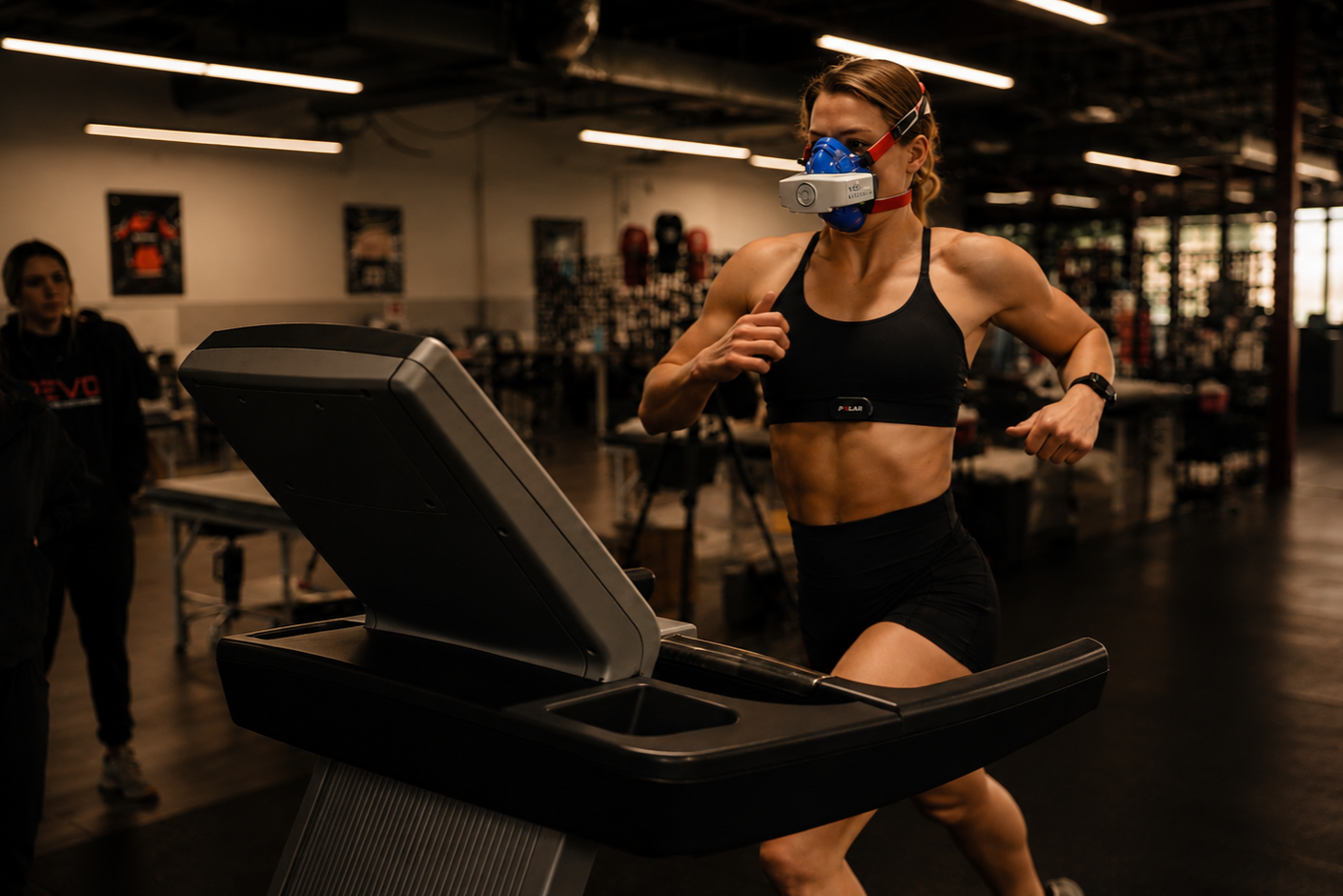 A woman wearing workout clothes and a face mask running on a treadmill in a gym.