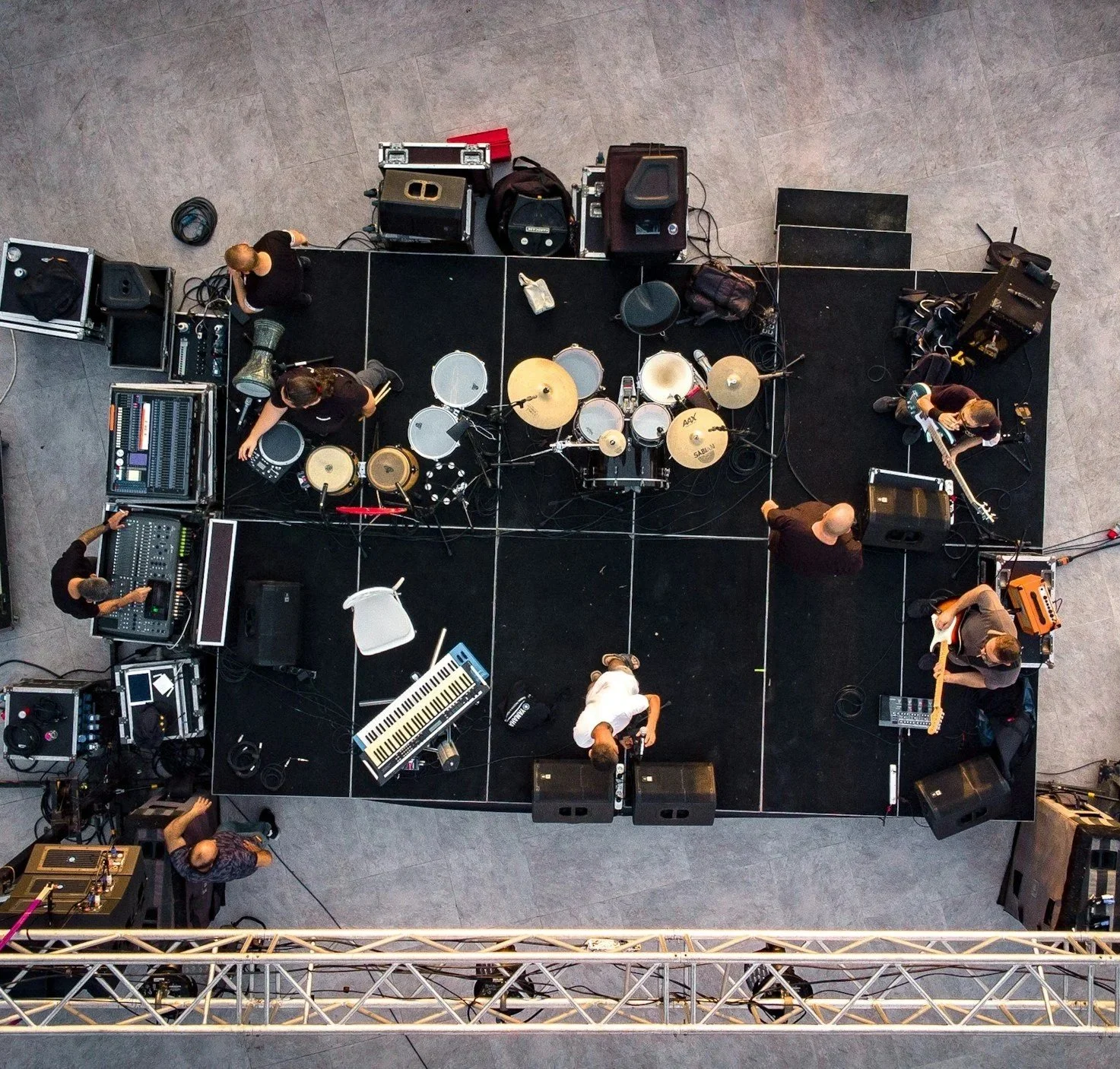 Top-down view of a music band setting up on stage with drums, keyboards, guitars, and sound equipment, preparing for a performance.
