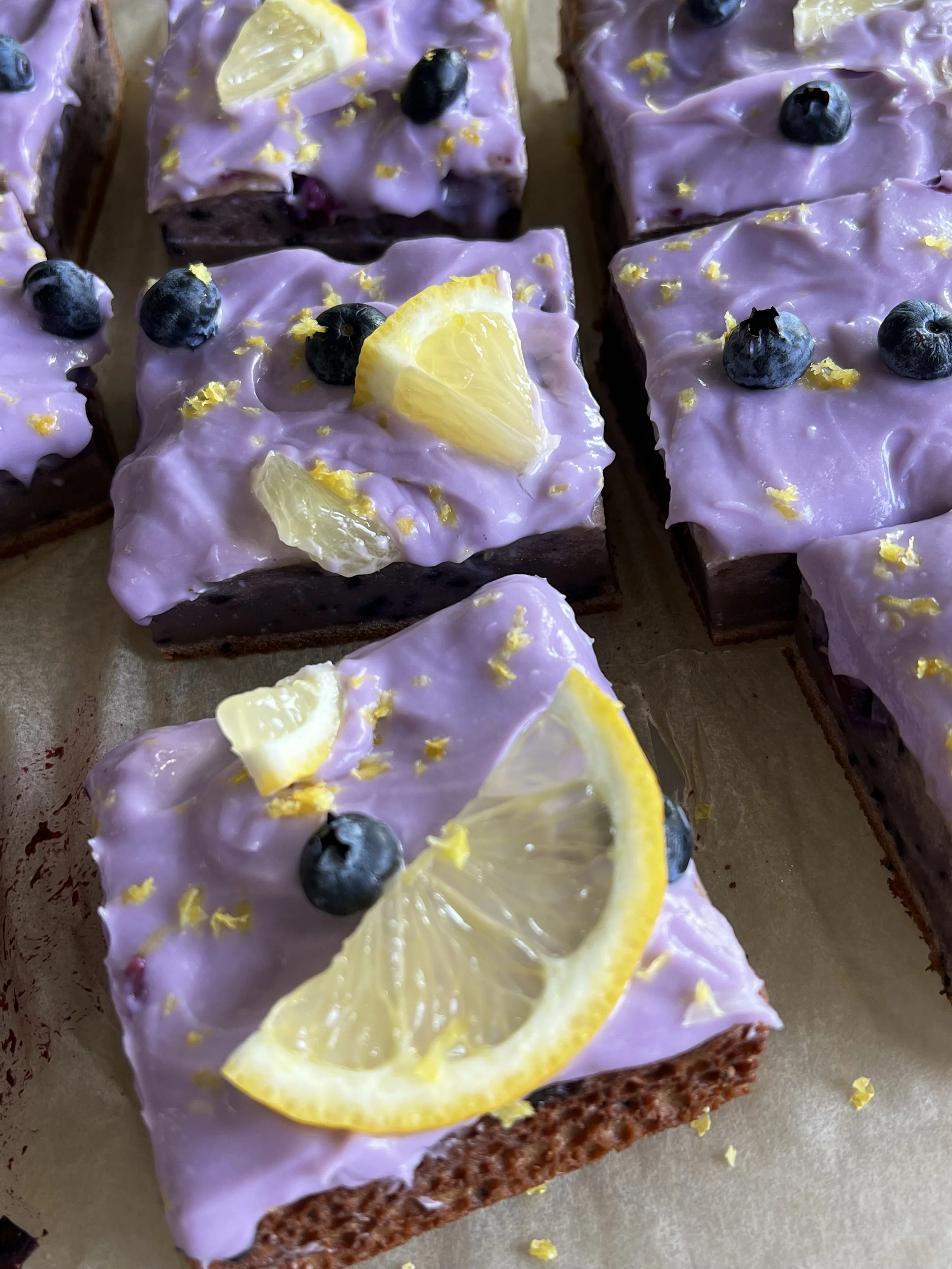 mochi blueberry bar slices with frosting, fresh blueberries, and lemon slices on top