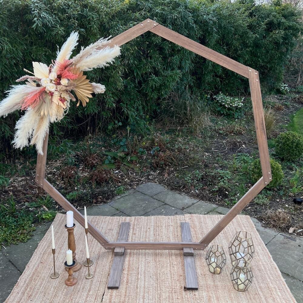 Boho/rustic heptagonal wooden arch, sat on jute rugs and dressed with pampas grass arrangement,  candlesticks and lanterns