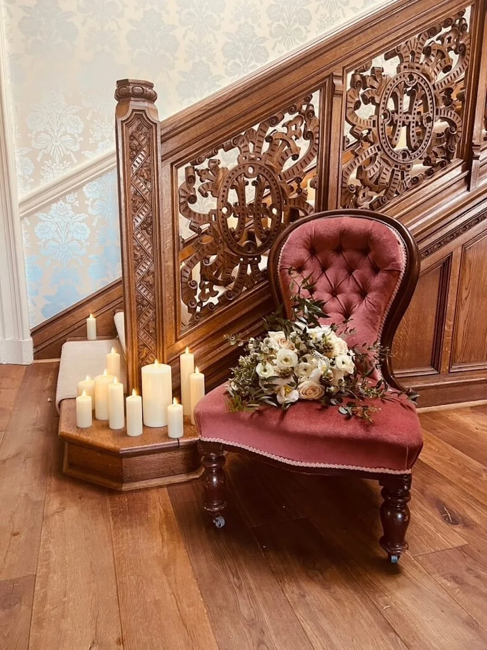 Antique, vintage spoonback nursing chair in pink velvet, dressed with the bride's bouquet and shown at the bottom of a dramatic staircase styled with flameless LED candles