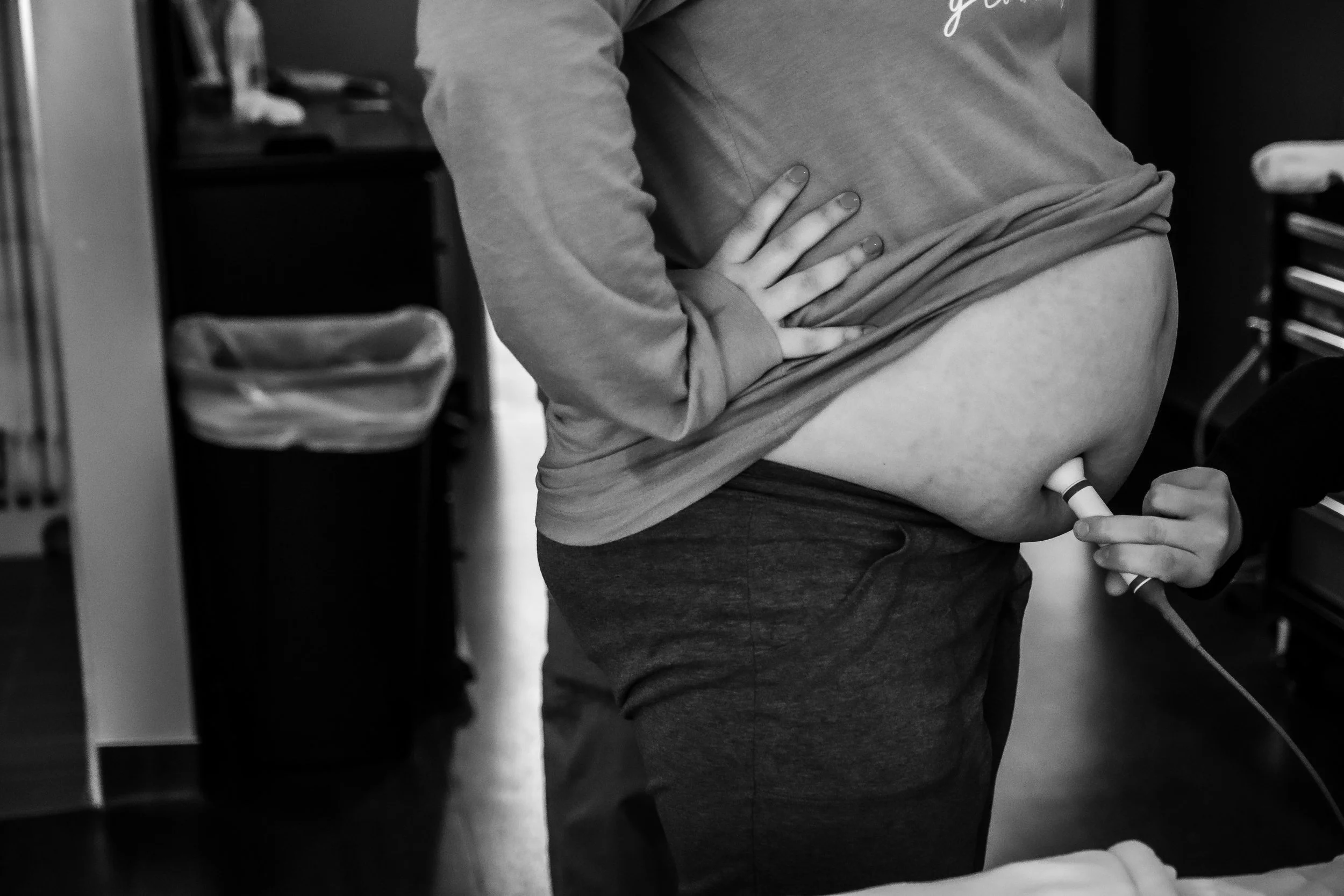 A person wearing a long-sleeve shirt and shorts, using an ultrasound device on their abdomen.