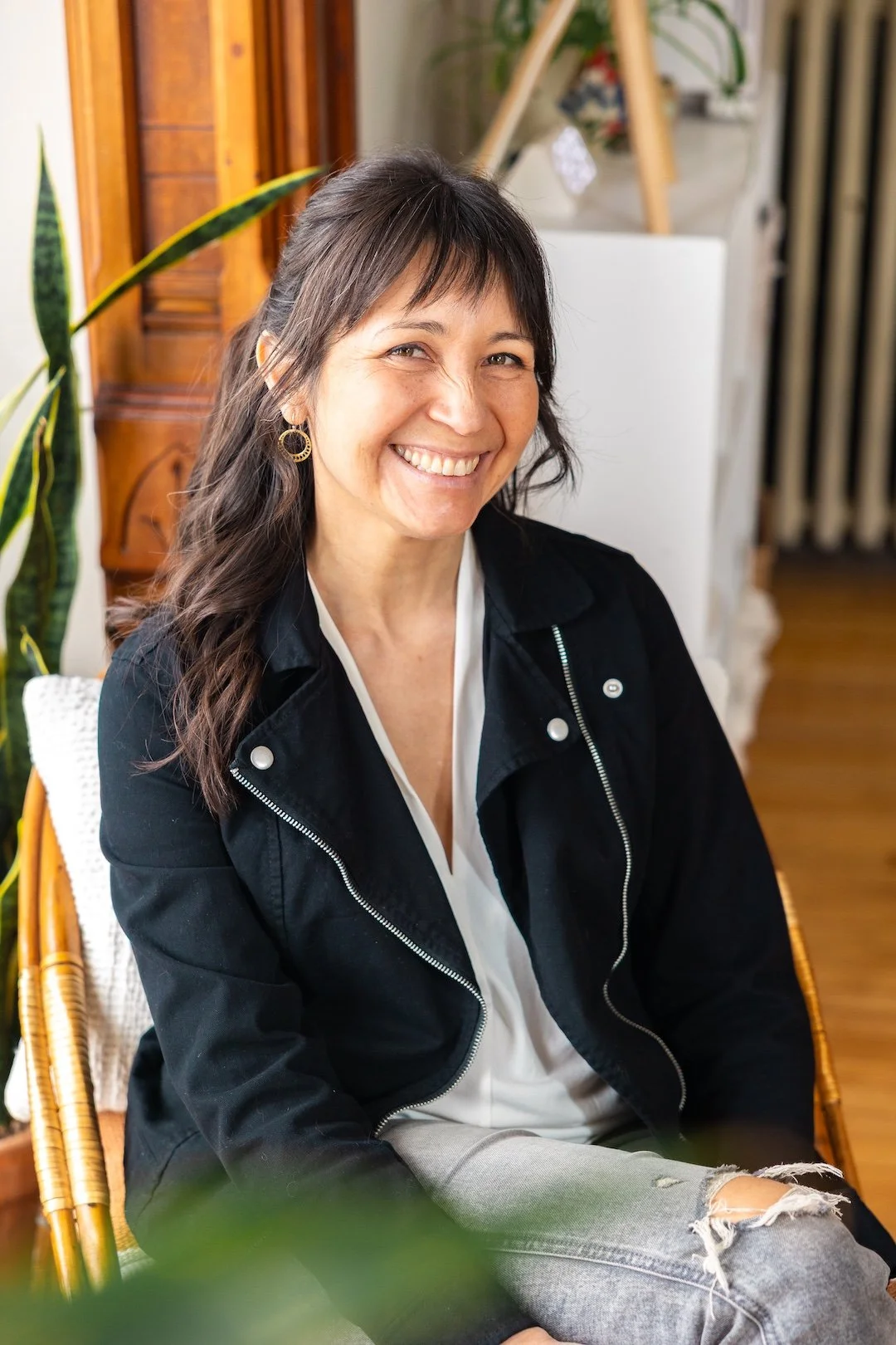 Ramona Hernandez, owner and designer at Wonder Web Creative, a Squarespace web design business based in Vermont. She's smiling and wearing a black jacket over a white top, sitting in a cozy indoor space with plants and wooden furniture.