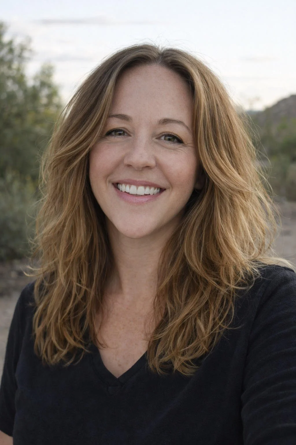 A woman with red hair smiling outdoors, wearing a black top.
